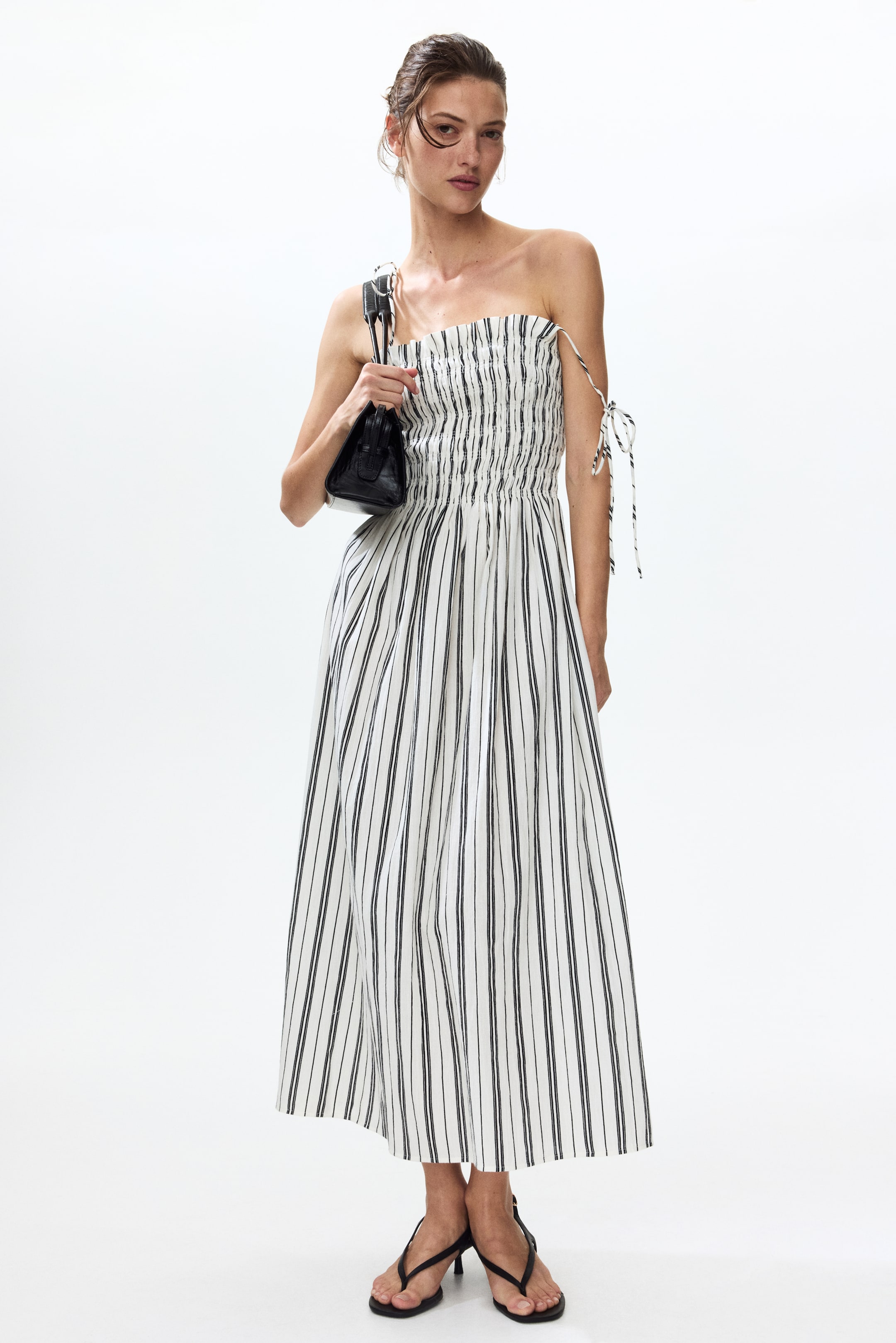View larger image: The strapless midi dress showcases white fabric adorned with black vertical stripes. It boasts a shirred bodice and a flowing skirt, complete with decorative ties emerging from the sides of the bustline.