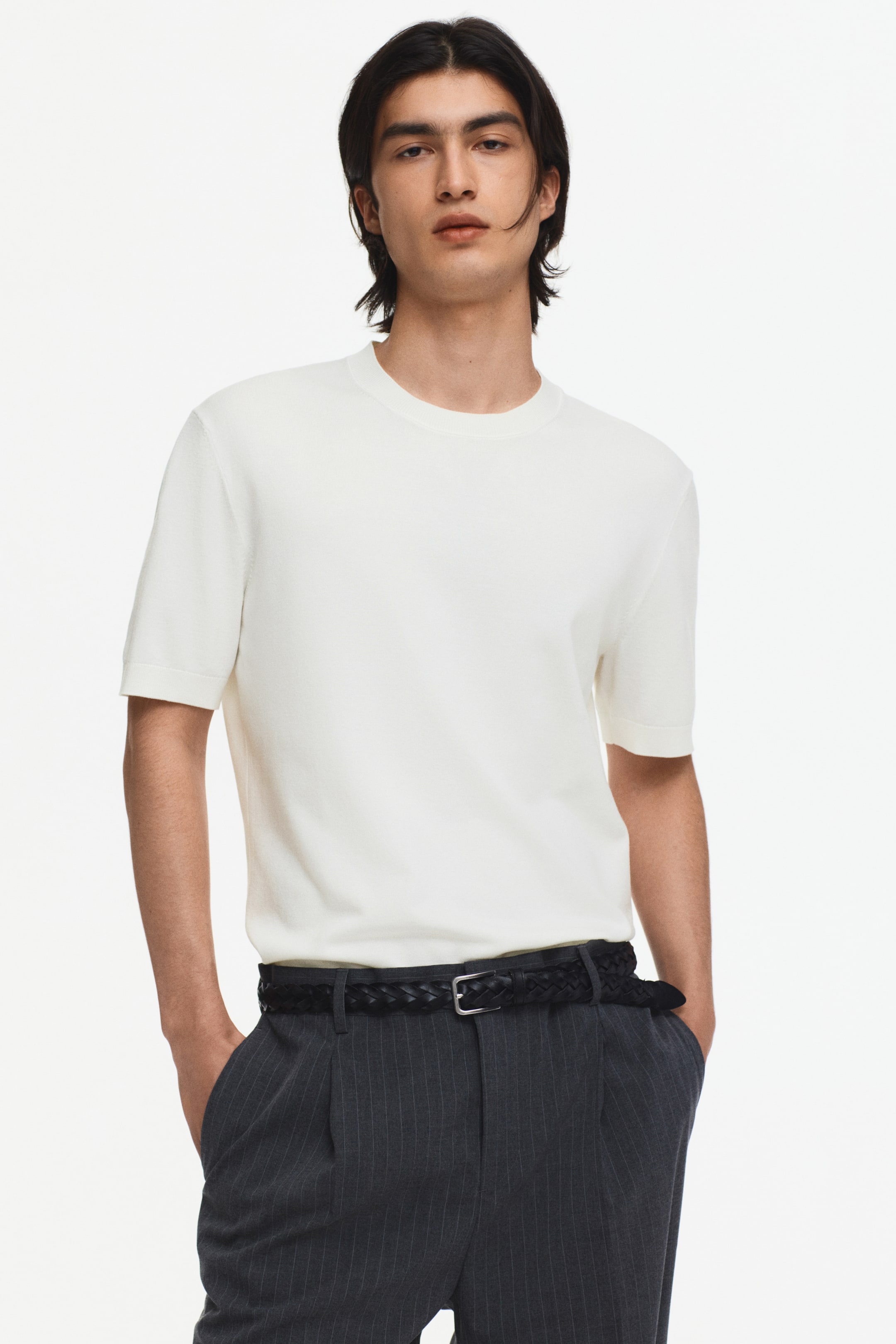 Ampliar la imagen: Un top de punto color crema de manga corta se presenta desde el frente, con un cuello redondo y dobladillos de las mangas acabados con limpieza. Se ajusta al cuerpo y se lleva metido dentro de pantalones oscuros.