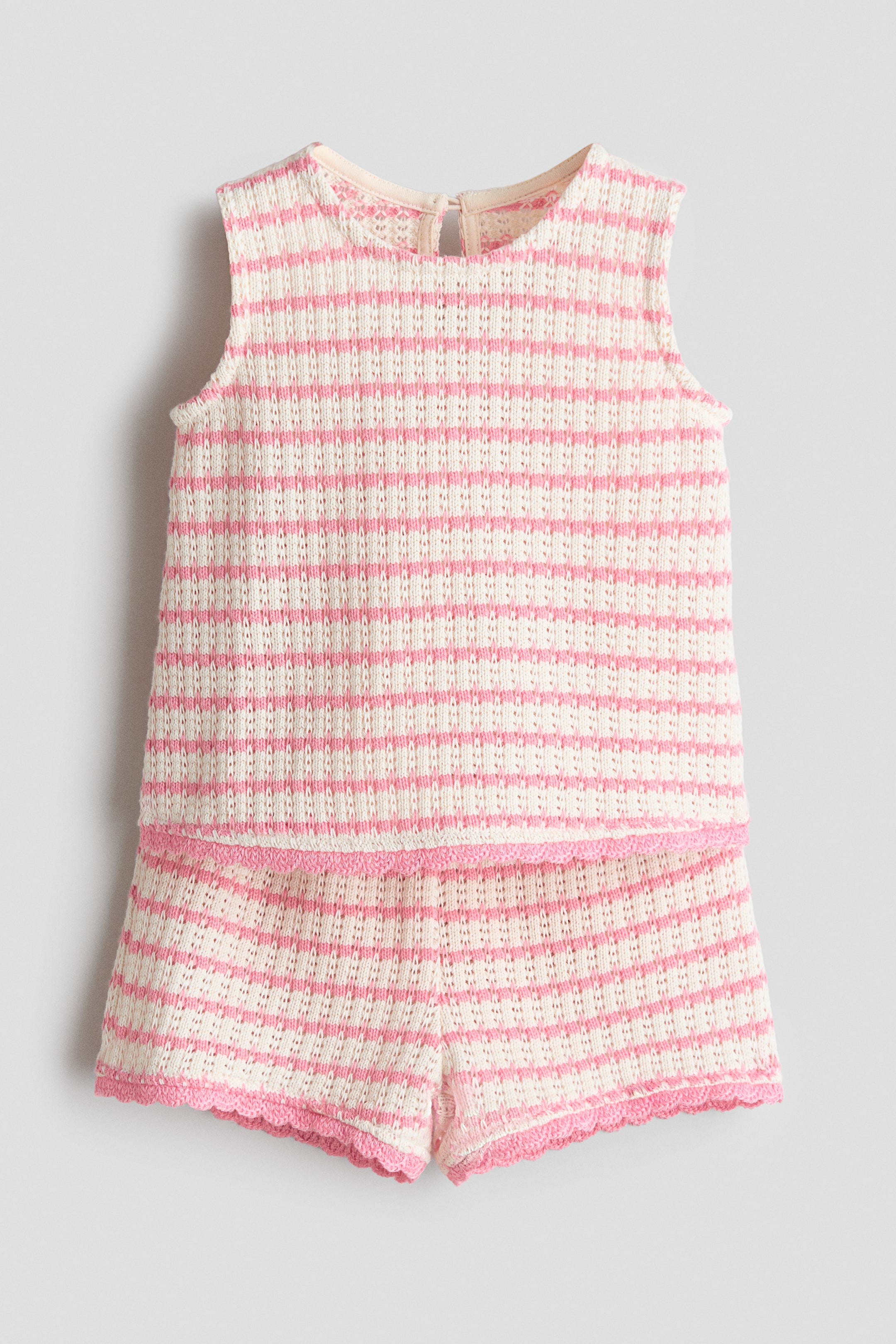 View larger image: A two-piece knitted ensemble showcases a sleeveless top paired with matching shorts in a cream hue adorned with horizontal pink stripes. The open-knit design highlights a round neckline and a keyhole opening at the back of the top, while the shorts are embellished with a pink scalloped trim along the leg openings.