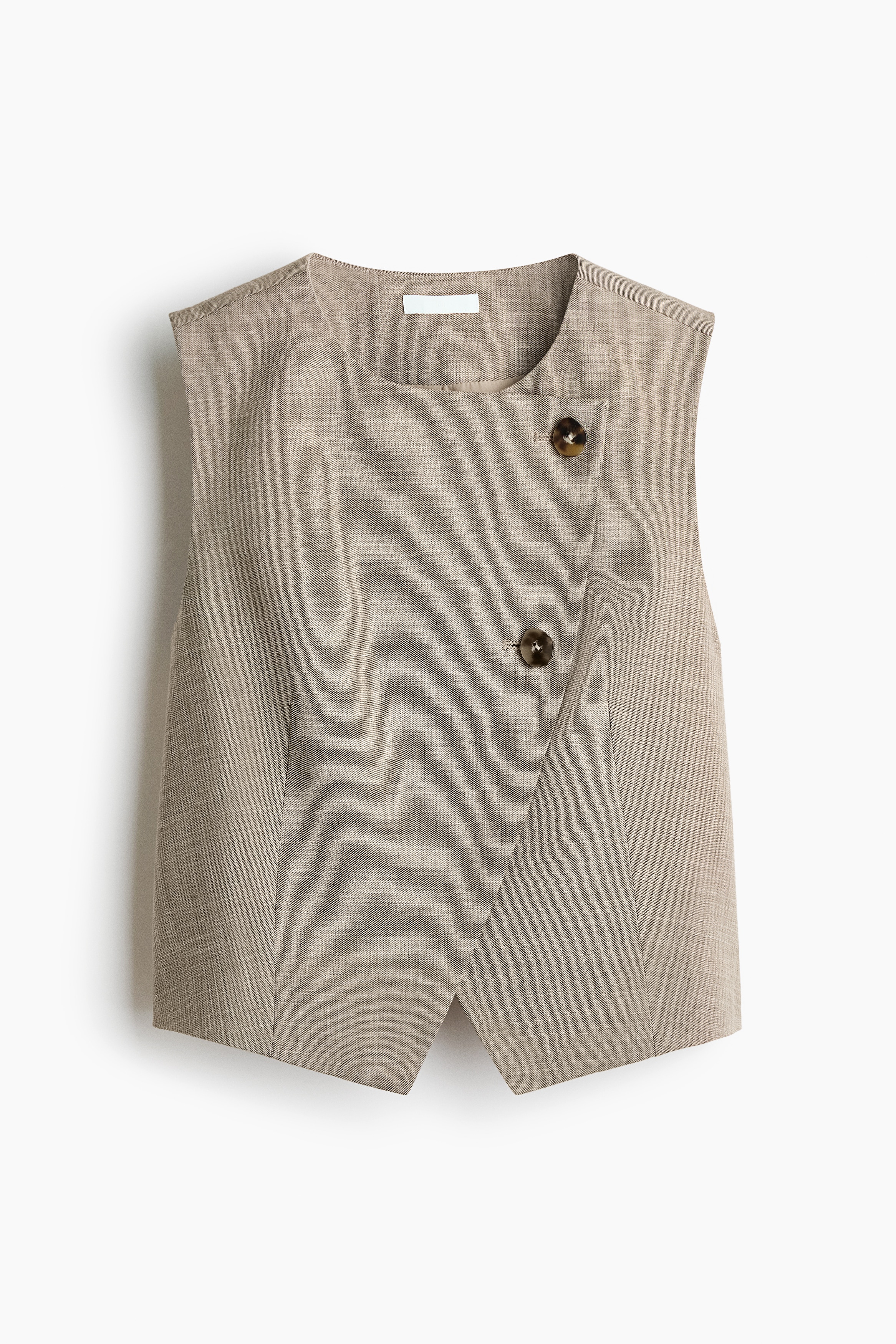 A beige, sleeveless woven vest featuring a round neckline and cropped hem is being worn by the model, who is standing in profile. The vest is paired with matching wide-leg trousers in the same fabric, with the model placing one hand in the trouser pocket.