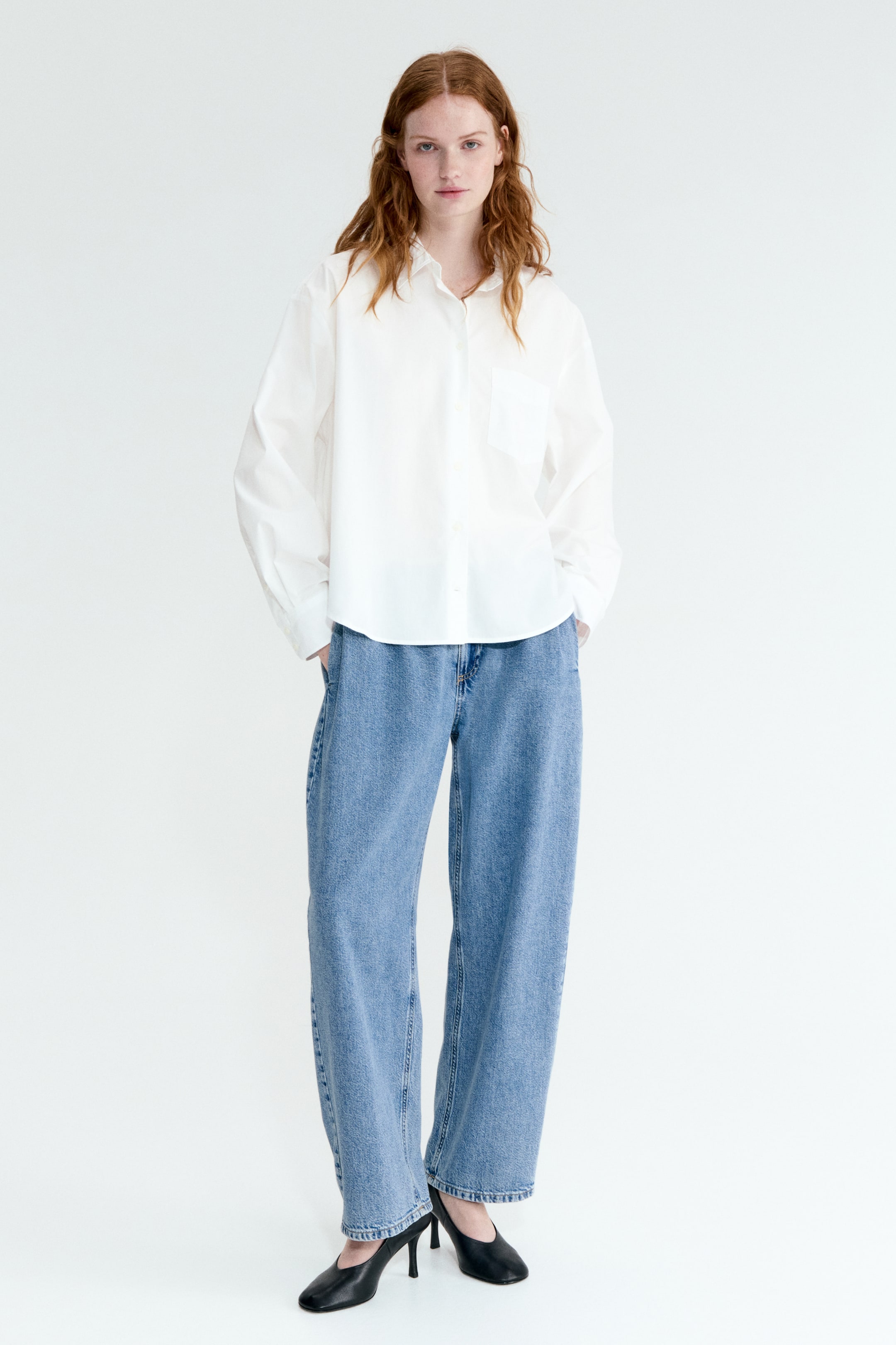 查看大圖: 白色寬鬆版扣襟襯衫，特色為尖領、長袖配有扣式袖口，以及胸前口袋，搭配淺藍色寬腿牛仔褲。