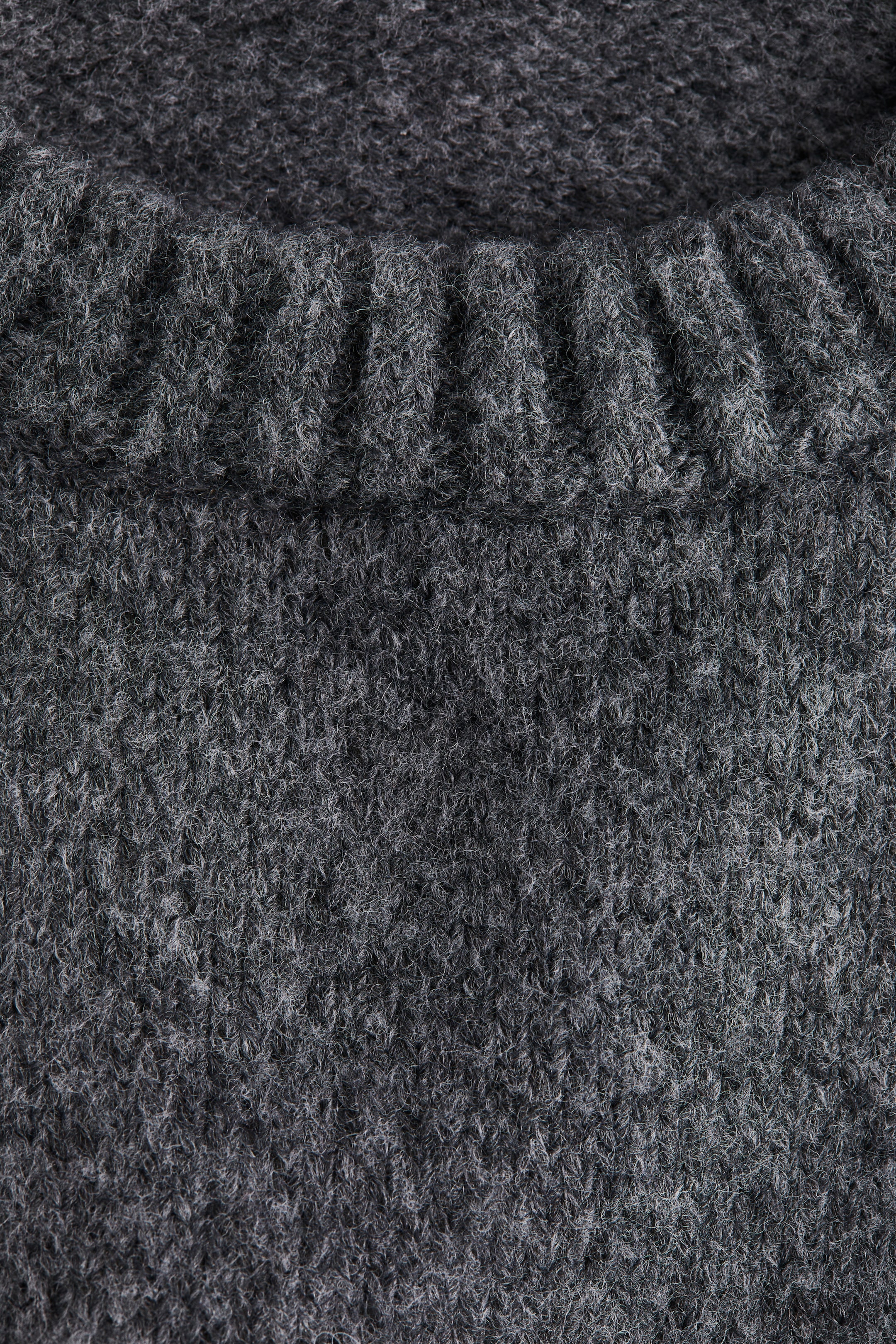 View larger image: A heathered gray sweater is presenting a close-up of its knitted fabric. The main body is displaying a uniform, slightly fuzzy knit, while the top portion is featuring a prominent ribbed neckline.