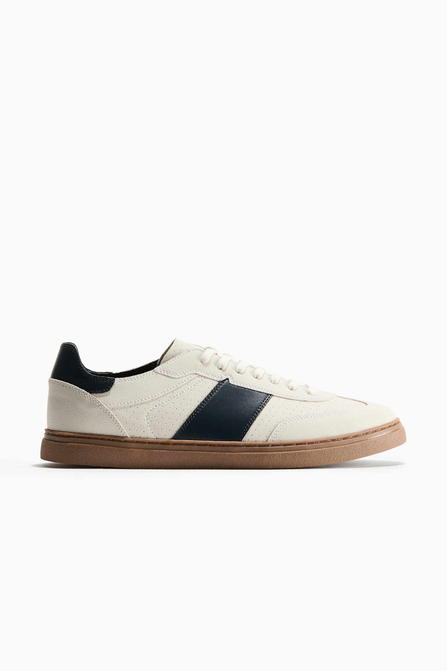 A low-top sneaker is shown facing right in a side profile view, showcasing a textured off-white upper with a prominent diagonal navy blue stripe on the side. The sneaker features a matching navy blue heel tab, off-white laces, and a textured brown gum sole.