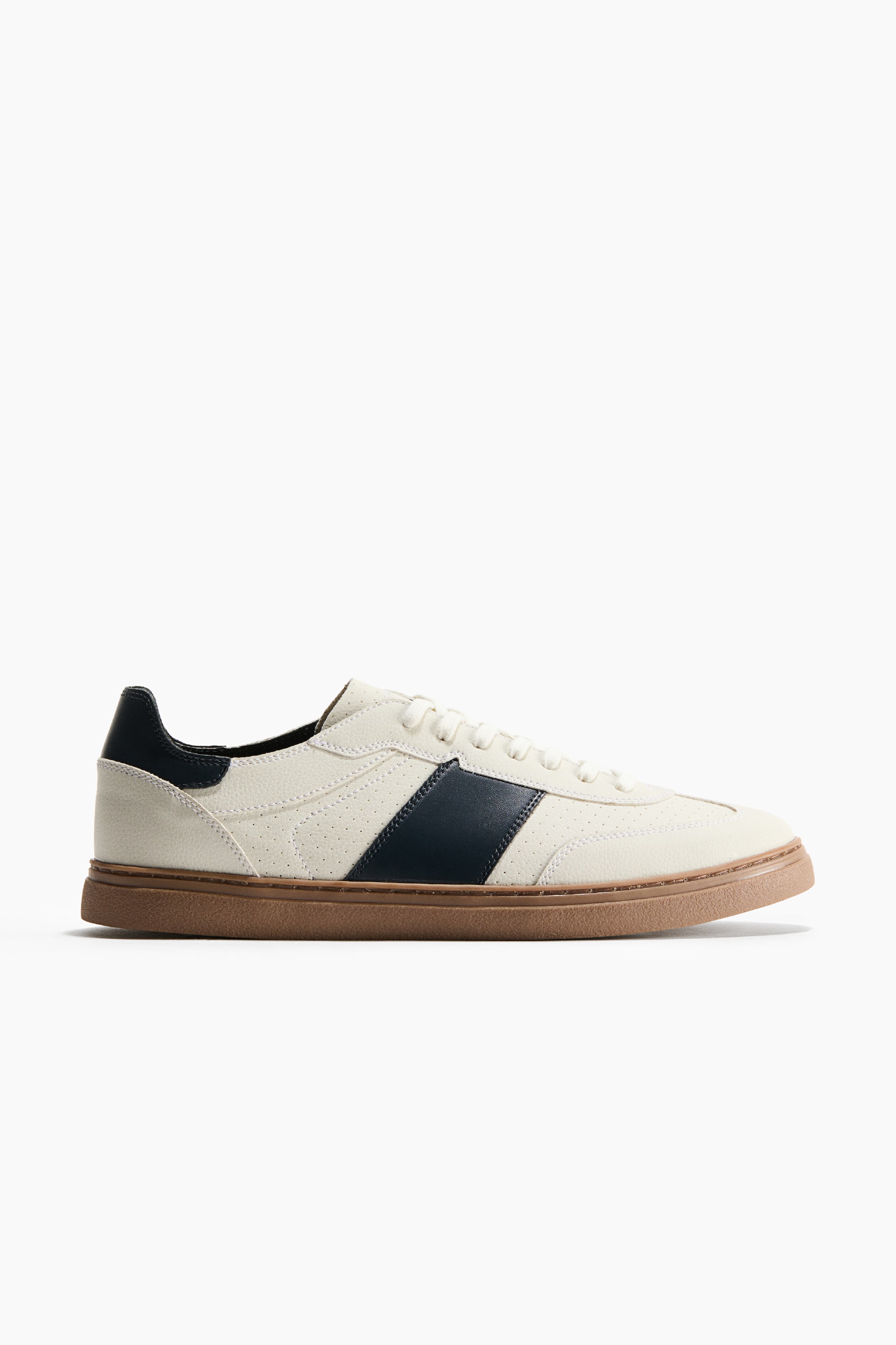 View larger image: A low-top sneaker is shown facing right in a side profile view, showcasing a textured off-white upper with a prominent diagonal navy blue stripe on the side. The sneaker features a matching navy blue heel tab, off-white laces, and a textured brown gum sole.
