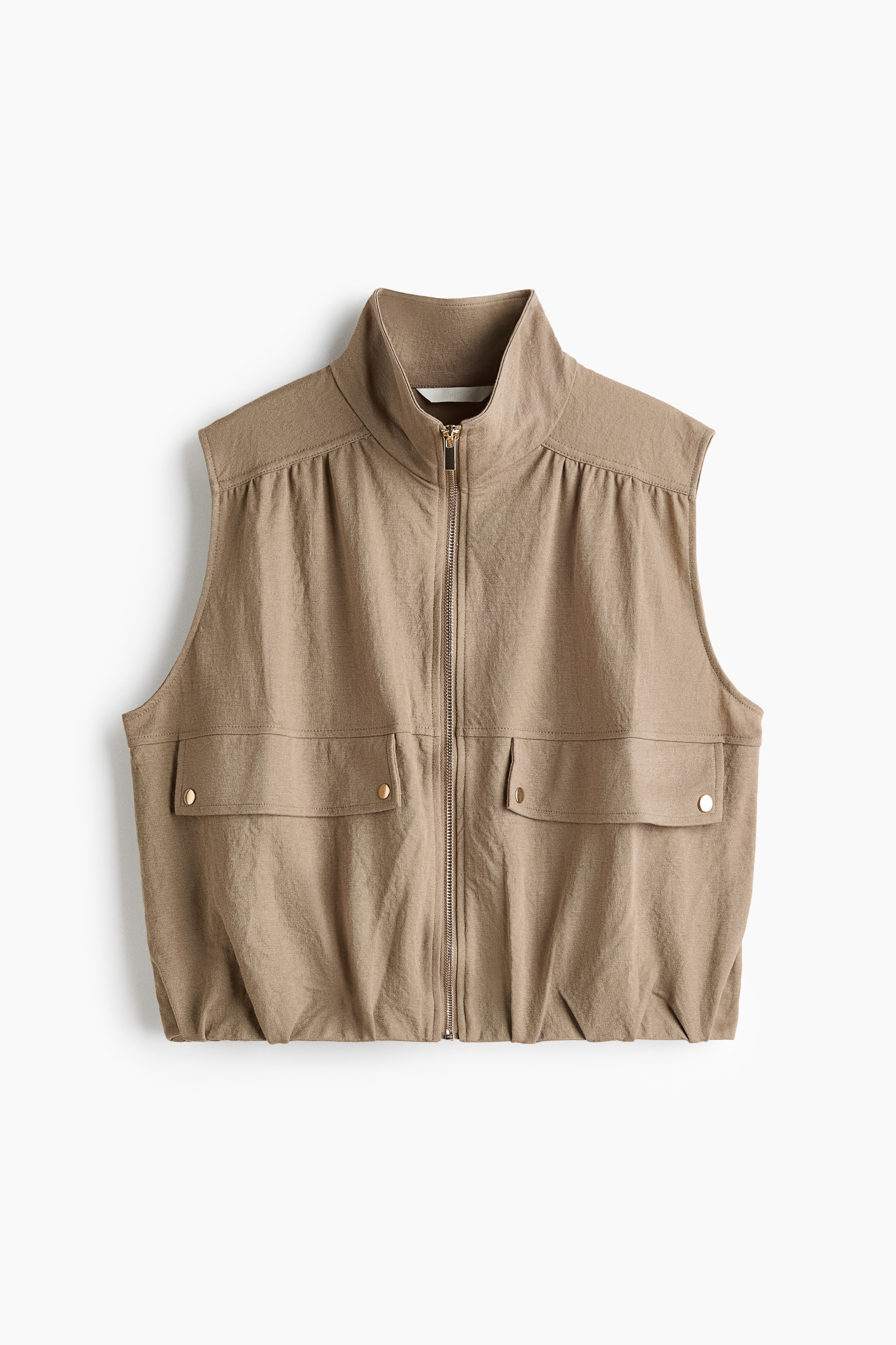 A light brown, woven viscose-blend vest is being worn by the model, featuring a high funnel collar and a gold-tone zipper down the front. The sleeveless design includes a gathered yoke over the shoulders and two front pockets with snap-button flaps.