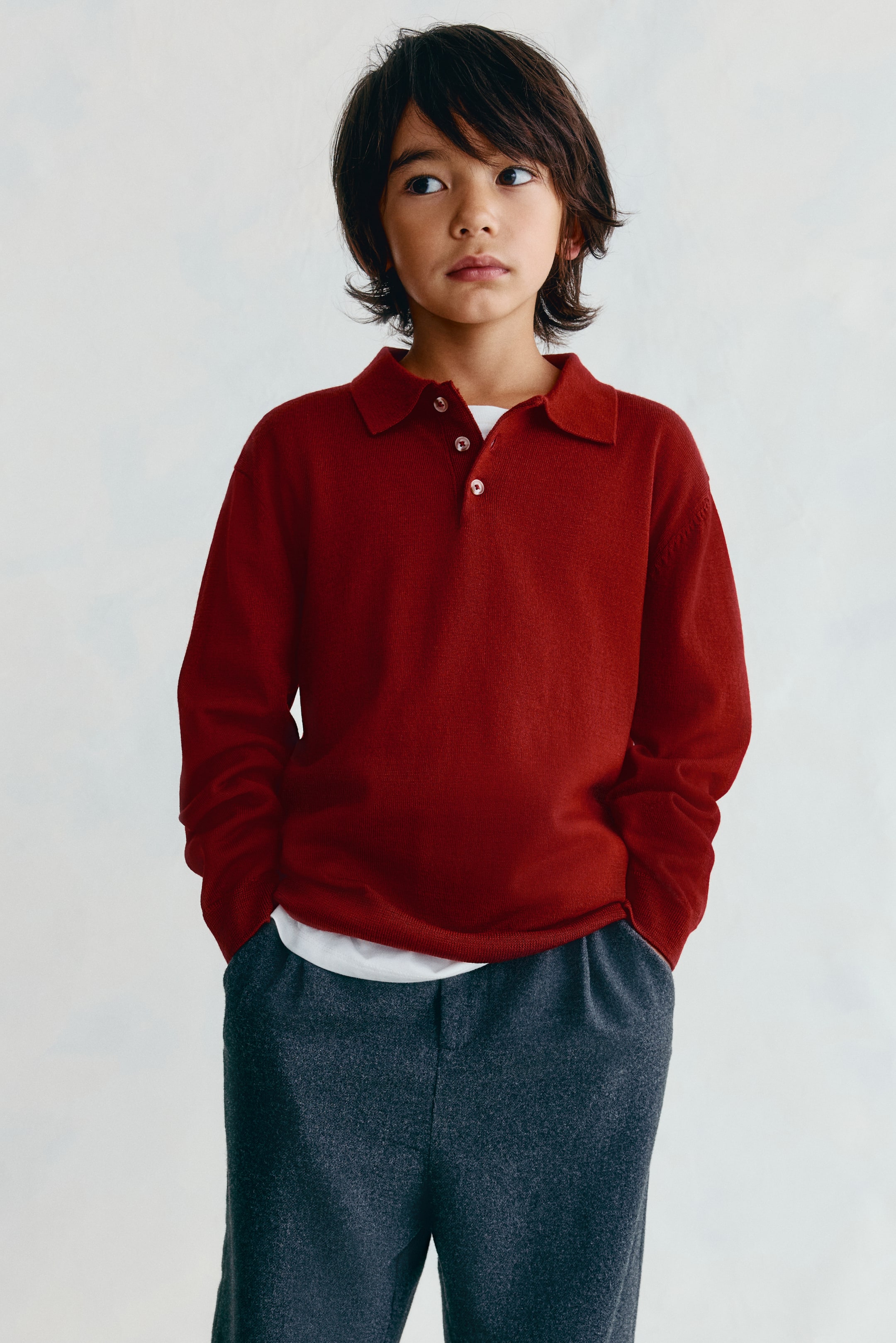 View larger image: A red fine-knit polo sweater features a turn-down collar, a button placket, and dropped shoulders in a front-facing view. The sweater is shown with long sleeves, ribbed cuffs, and a ribbed hem, layered over a white T-shirt.