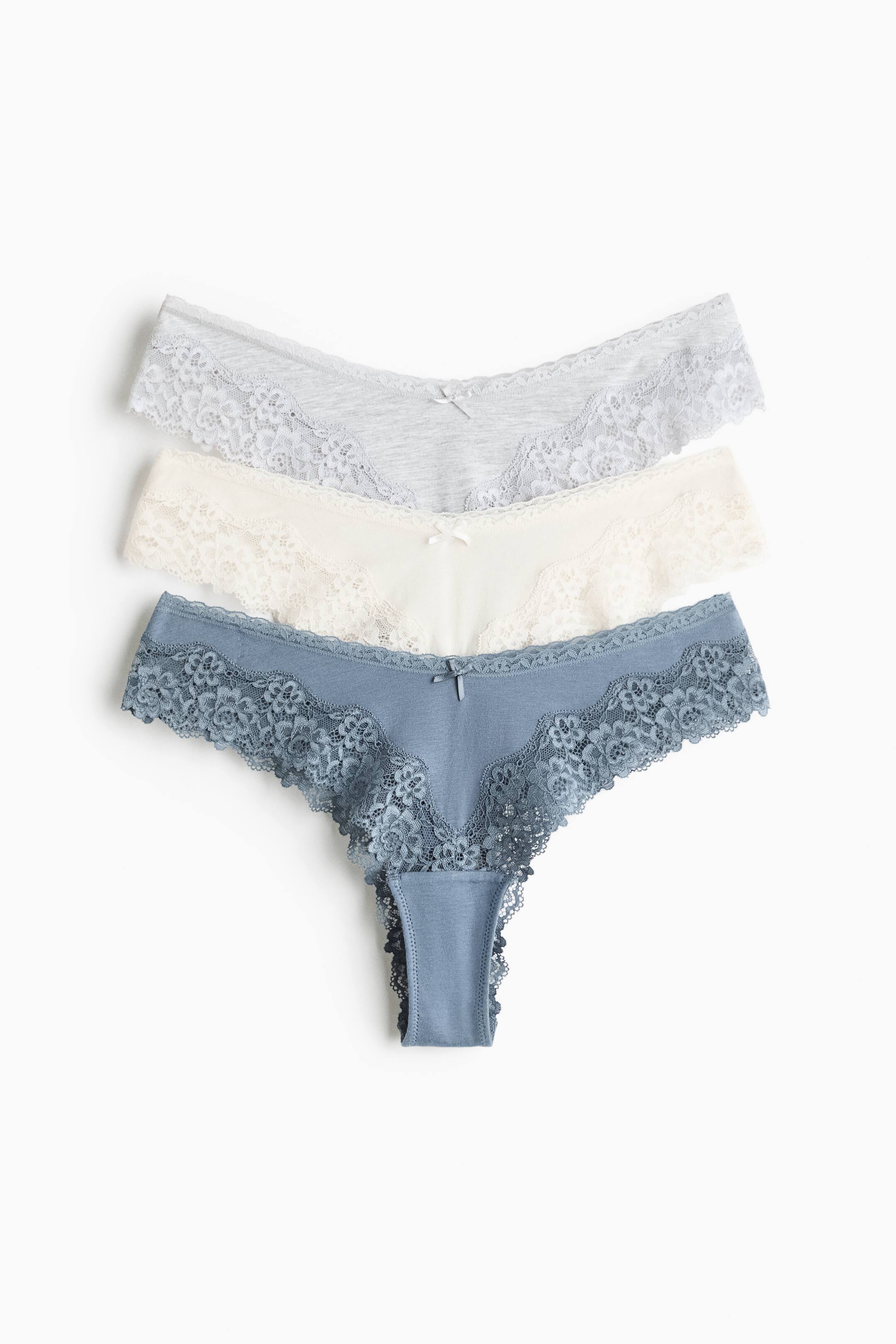 Grotere afbeelding bekijken: Drie paar lage slips in lichtgrijs, crème en stoffig blauw liggen plat in een gestapelde opstelling, waarbij de voorzijde zichtbaar is. Elk paar heeft een body van katoenjersey met een V-vormige taille, een klein decoratief strikje in het midden en brede, geschulpte kanten inzetstukken aan de zijkanten.