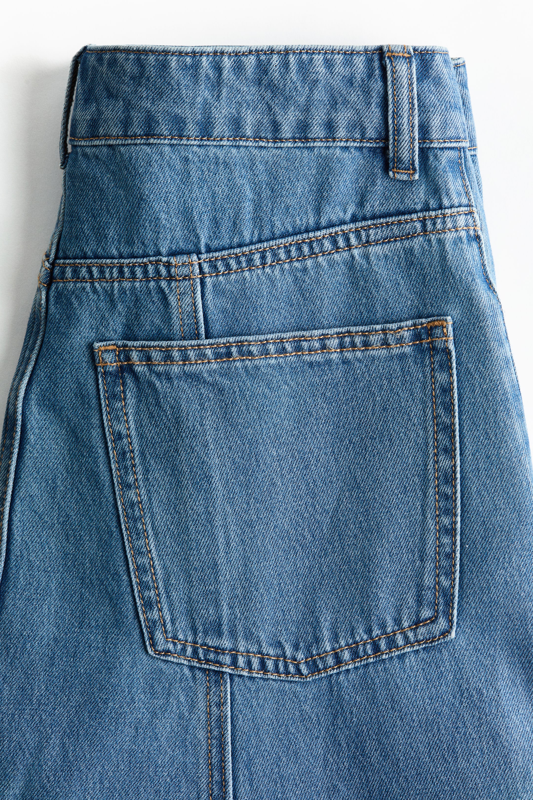 View larger image: Blue denim jeans are facing FRONT, displaying their back details. A waistband with belt loops is visible above a yoke, and a rectangular back patch pocket is appearing on the right, all outlined with contrast stitching.
