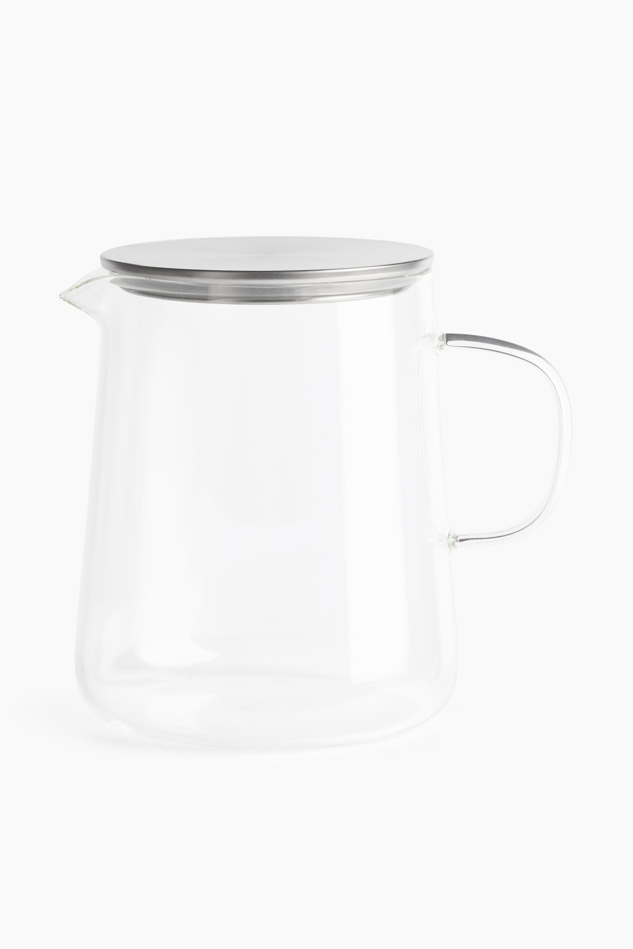 View larger image: A clear glass pitcher is shown from a front angle, featuring a slightly tapered body, a small integrated pouring spout on the left, and a thin, curved glass handle on the right. The pitcher is topped with a flat, circular, brushed-metal lid.