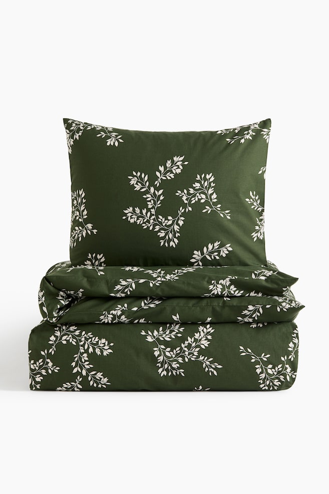 A dark green bedding set featuring a white botanical branch pattern is shown facing front, with a rectangular pillowcase standing upright on top of a neatly folded duvet cover. - 1