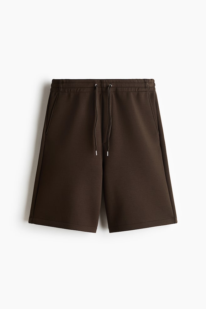 The dark brown shorts feature an elasticized waistband with a drawstring and silver-toned aglets, two side seam pockets, and a straight hem. - 1