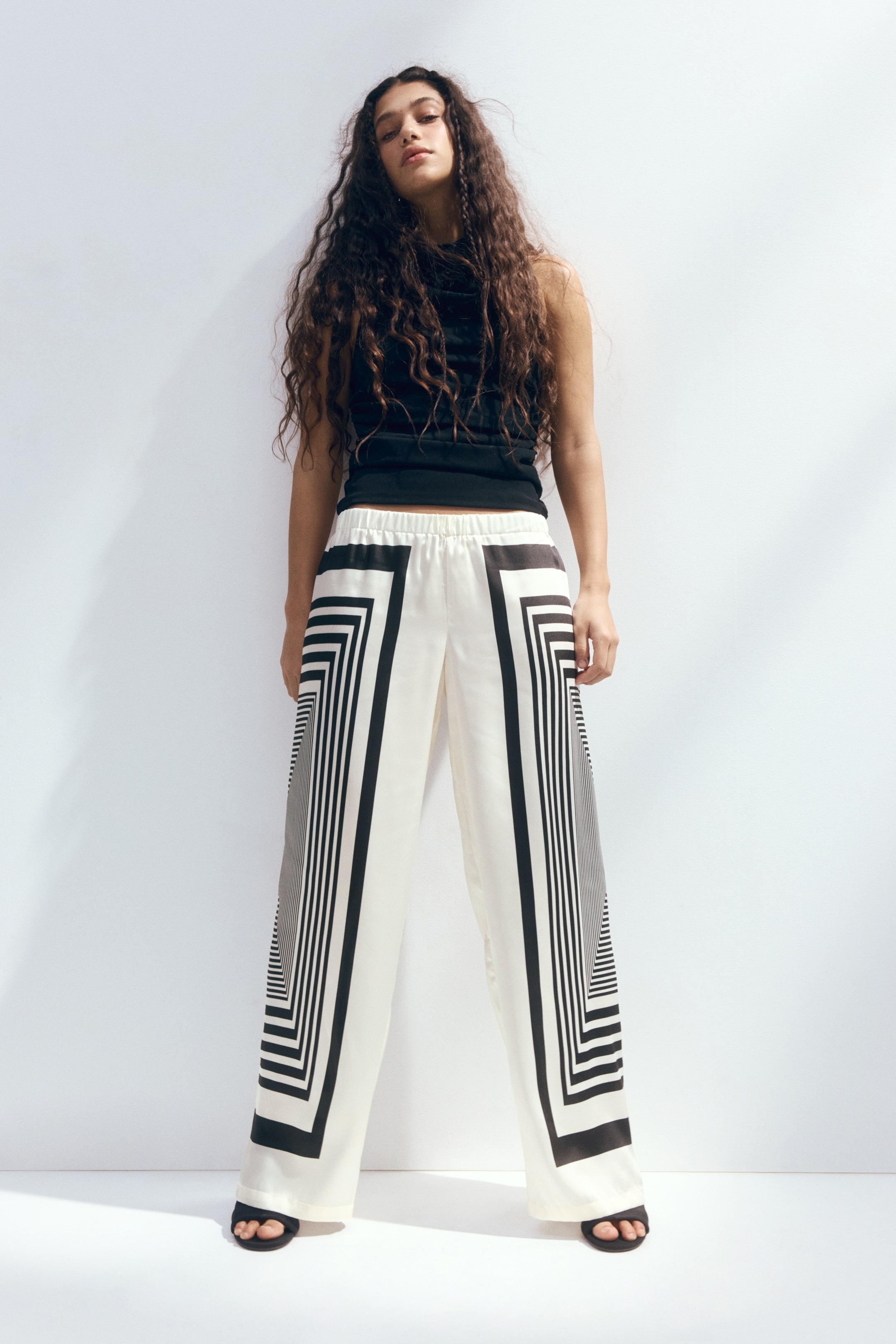 View larger image: The wide-leg trousers feature an elasticated waistband and a white base with a black geometric pattern of concentric rectangles running down the front and sides of each leg, creating an optical illusion.