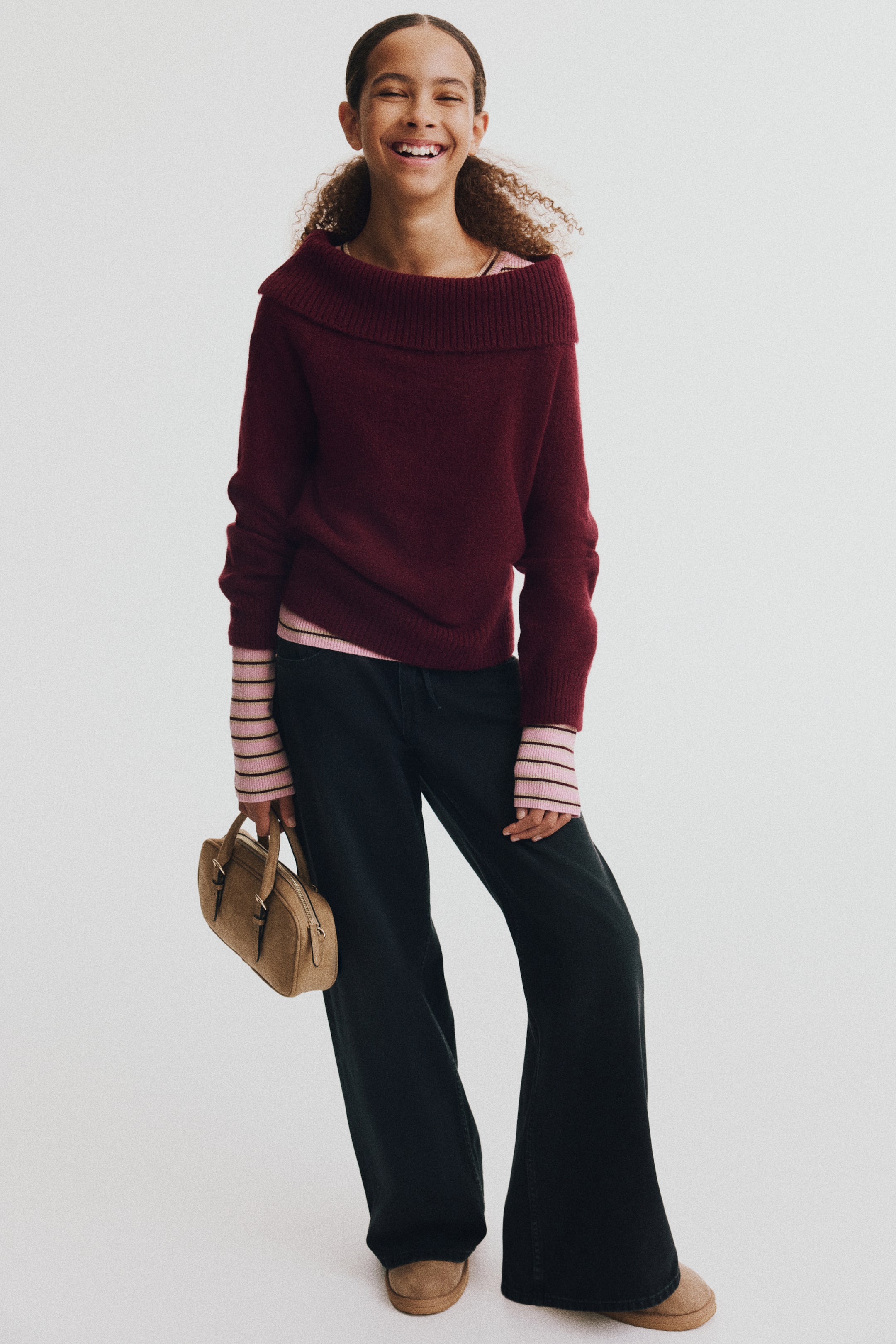 View larger image: A burgundy sweater in a soft knit is shown from the front, featuring a wide ribbed foldover collar, long sleeves, and ribbing at the cuffs and hem. The sweater is layered over a pink-and-black striped top, which peeks out at the neckline, cuffs, and hem.
