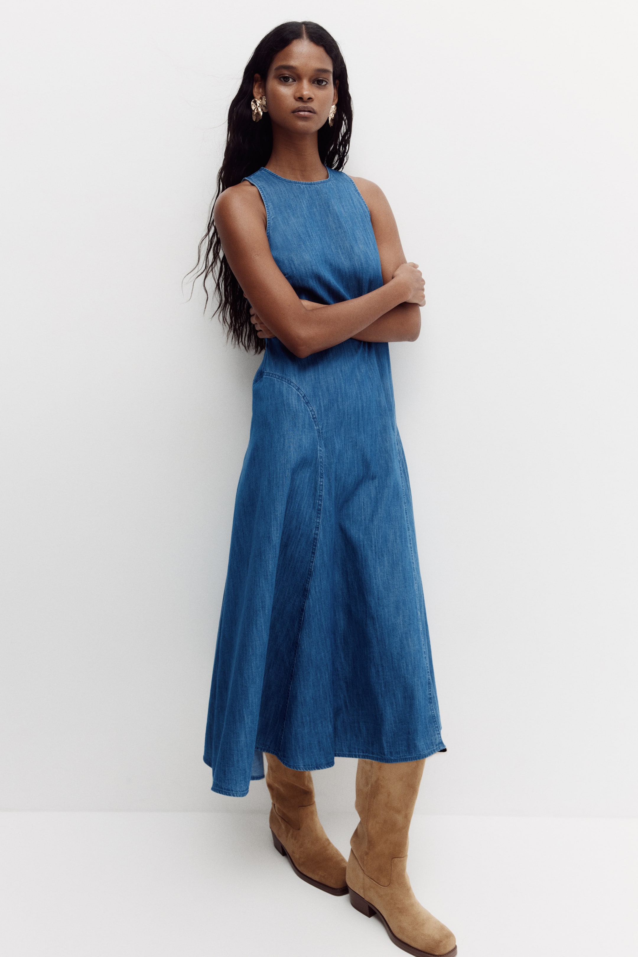 View larger image: The sleeveless denim midi dress features a round neckline and a fitted bodice, flowing into an A-line skirt with visible vertical seams, shown from a slightly angled front view.