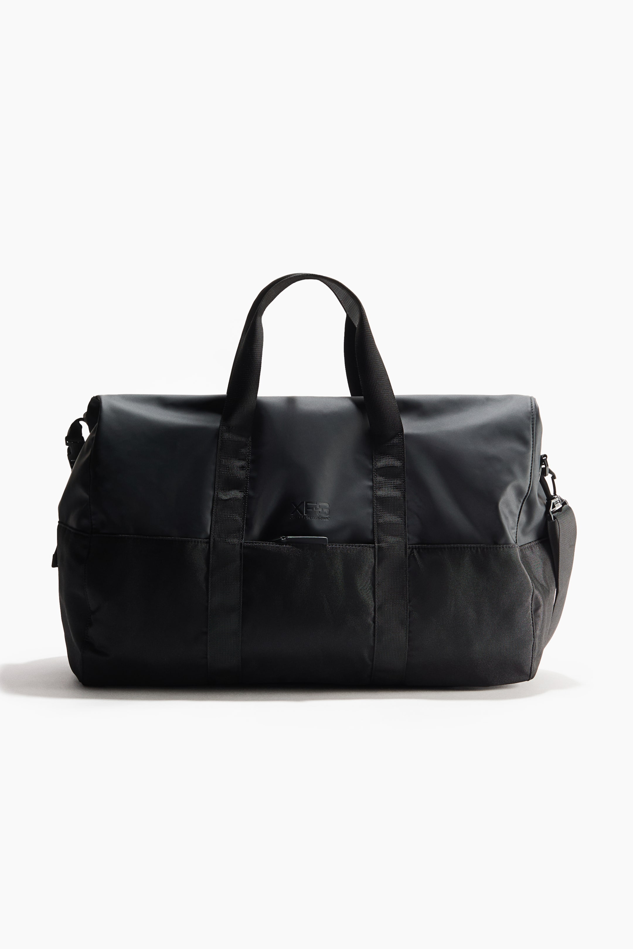View larger image: A black duffel bag is shown from the front, featuring a smooth upper section and a textured lower section. It includes two top webbing carry handles, a detachable webbing shoulder strap, a small embossed logo, and a zippered pocket at the front.