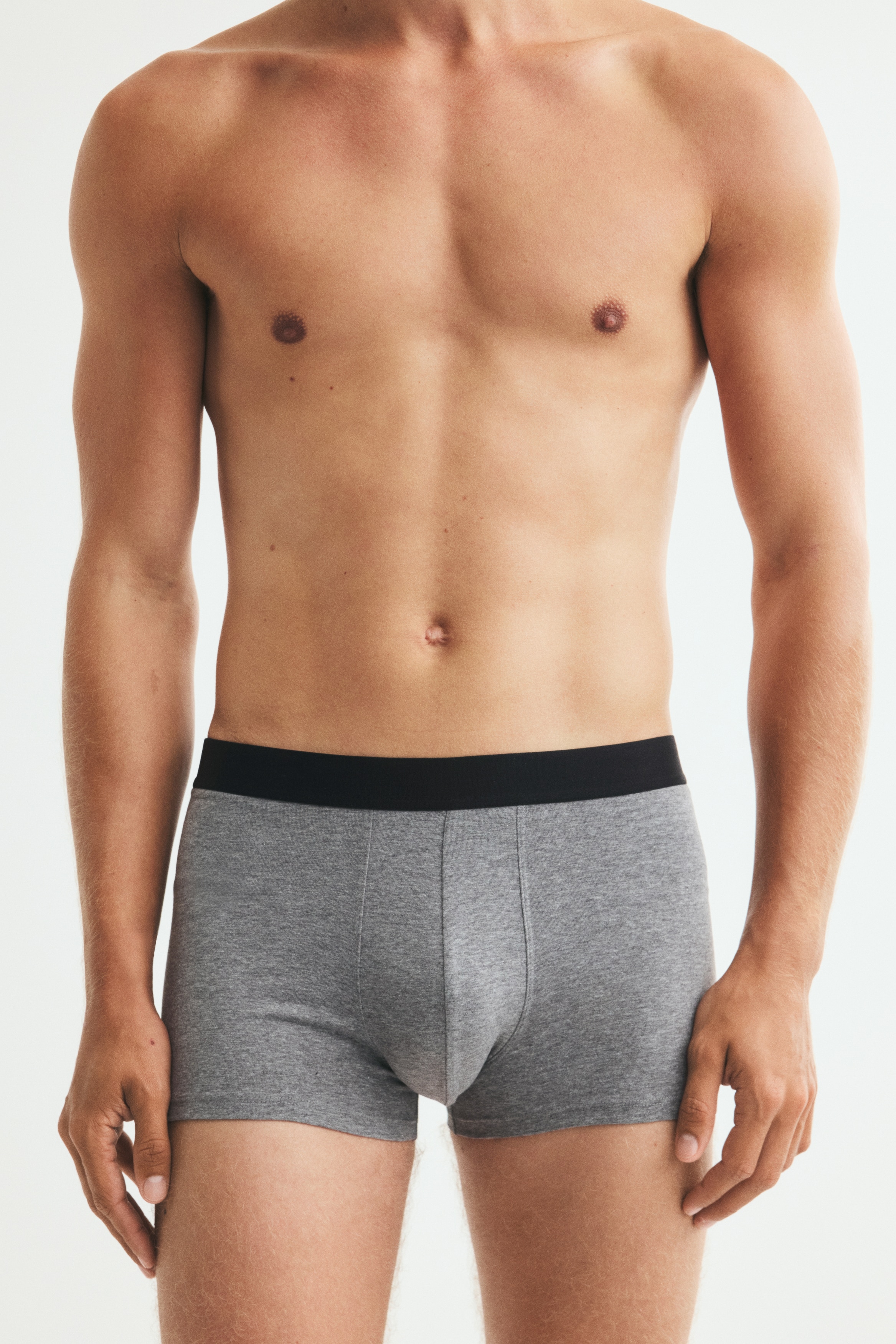 Five pairs of boxer briefs are presented in a stacked and fanned arrangement, with the front of the top pair facing forward. The pairs are varying in shades of heathered grey and solid black, each featuring a contrasting black elastic waistband. The visible light grey pair on top is showing a contoured front pouch with central stitching.