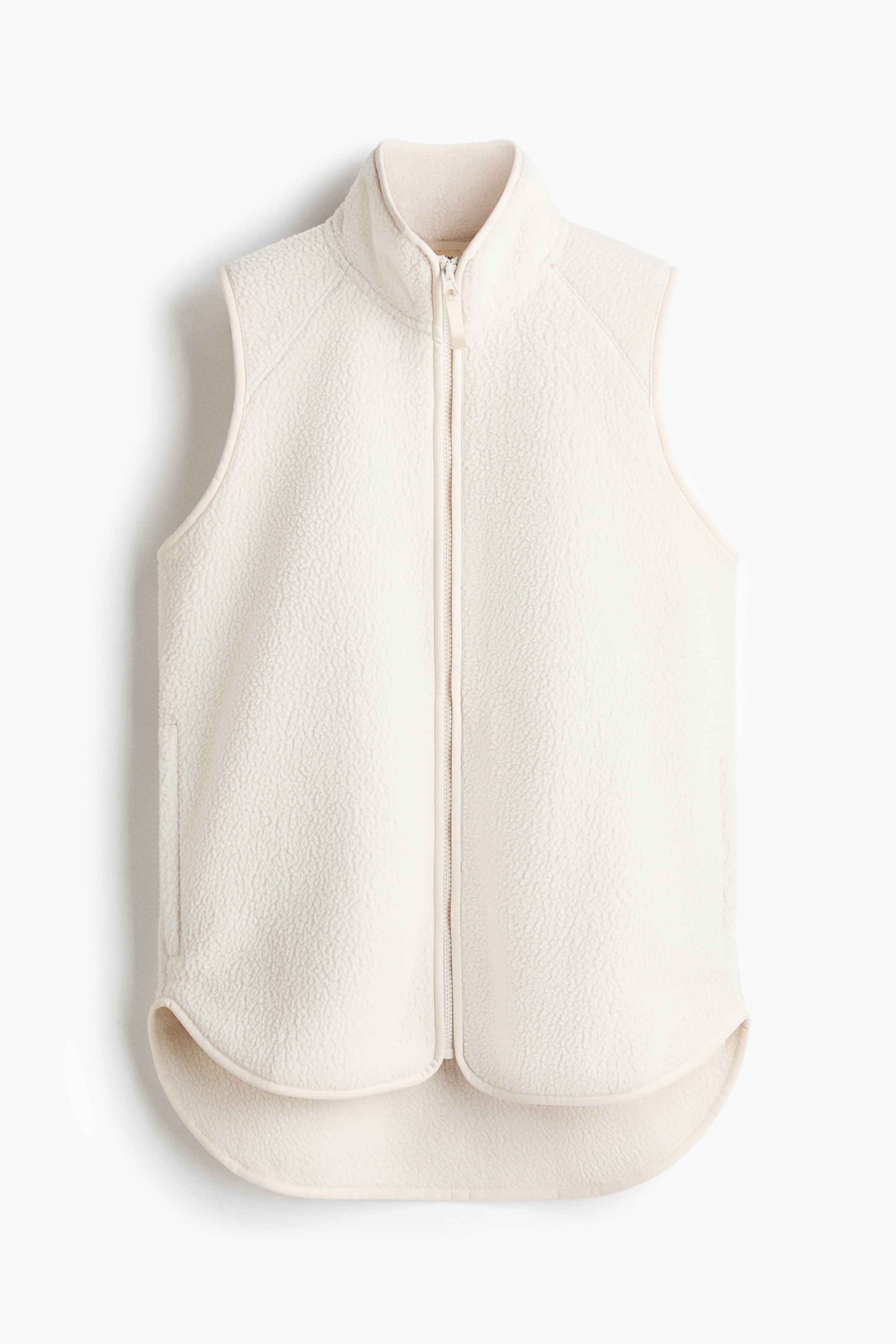 View larger image: A cream-colored fleece vest is presented front, featuring a high stand-up collar and a full-length zipper closure with a zipper pull. It is sleeveless, showing a rounded, dropped hemline and subtle side pockets.
