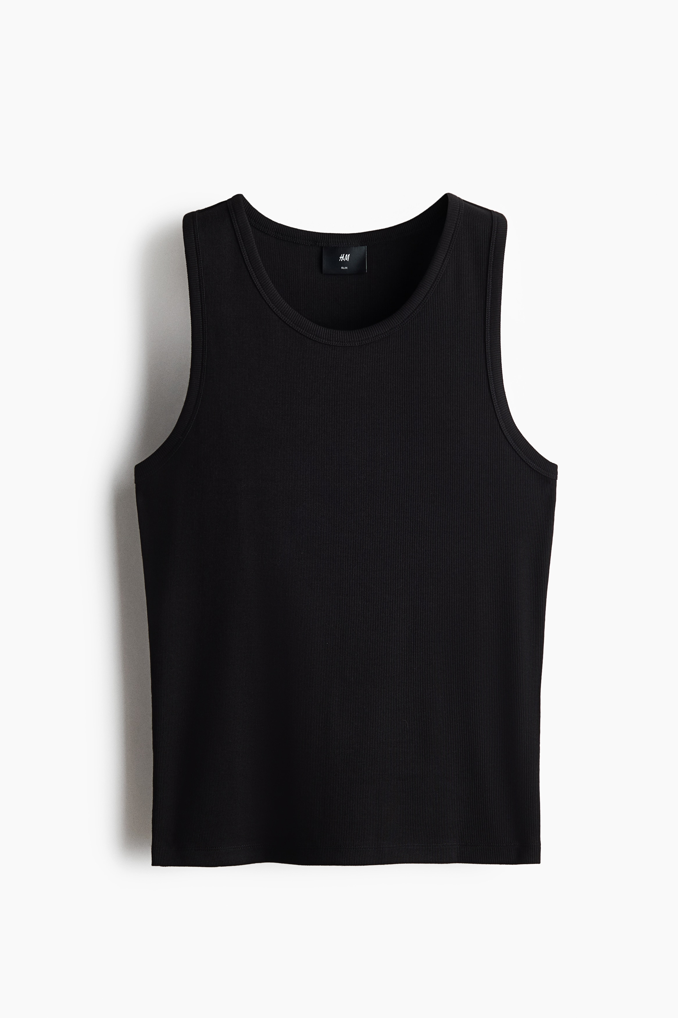 The model is wearing a black ribbed cotton jersey tank top, featuring a slim fit and a round neckline. The tank top is styled with dark-wash denim jeans.