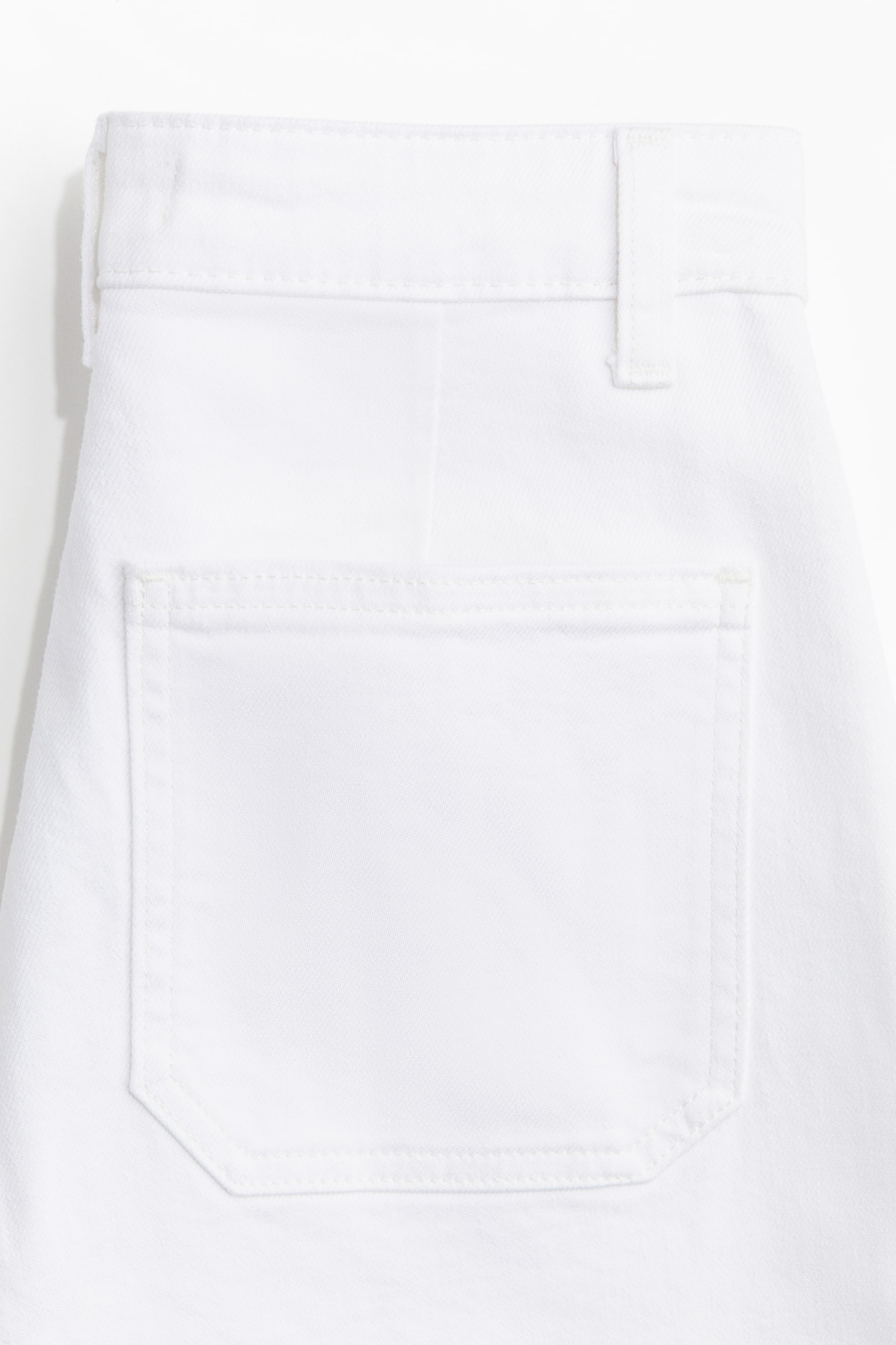 Visualizza immagine più grande: I pantaloni bianchi sono presentati dal retro, con una cintura piatta e un passante per cintura visibile sulla destra. Una tasca a toppa pentagonale è cucita sulla parte superiore sinistra del retro, dettagliata con cuciture visibili lungo i suoi bordi.