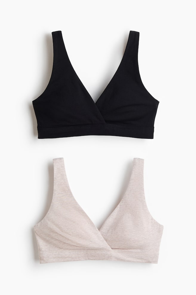 Two wireless cotton nursing bras, one in black and the other in heathered light beige, are being shown from the front. Both bras are featuring a crossover wrap-front design, wide shoulder straps, and a wide underband. - 1