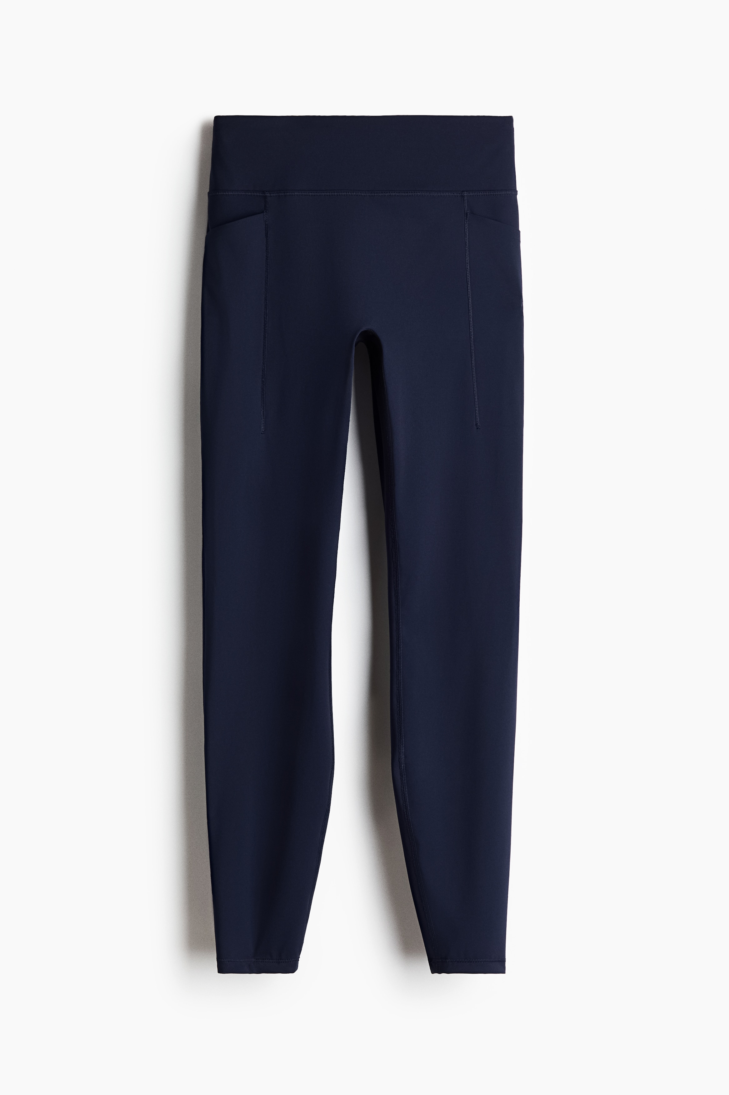 Un gilet noir sans manches Ã  fermeture Ã©clair, dotÃ© dâun col montant et dâun ourlet Ã  cordon de serrage, est portÃ© par le mannequin. Le gilet est superposÃ© Ã  une chemise blanche Ã  manches longues et agencÃ© avec des leggings bleu marine et des chaussures de sport blanches.