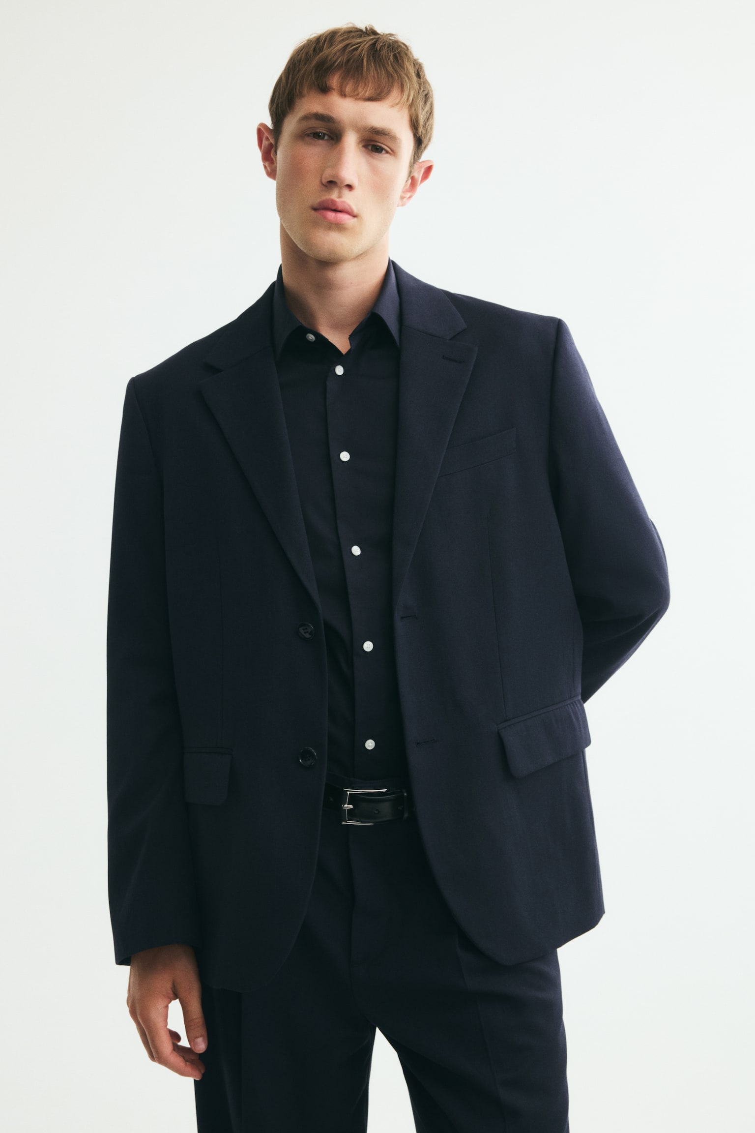 En mørkeblå blazer præsenterer sin front med notch-revers, en to-knaps lukning og en brystlomme med paspolering. Den viser også to klaplommer ved hofterne og fire dekorative knapper på hver manchet. - 1