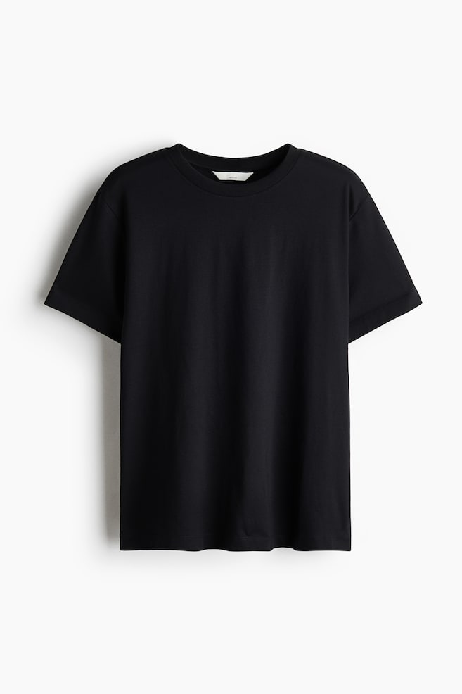 En sort T-shirt i bomuldsjersey hÃ¦nger med forsiden frem og viser en rund halsudskÃ¦ring med ribkant, korte Ã¦rmer og en lige skÃ¥ret sÃ¸m. - 1
