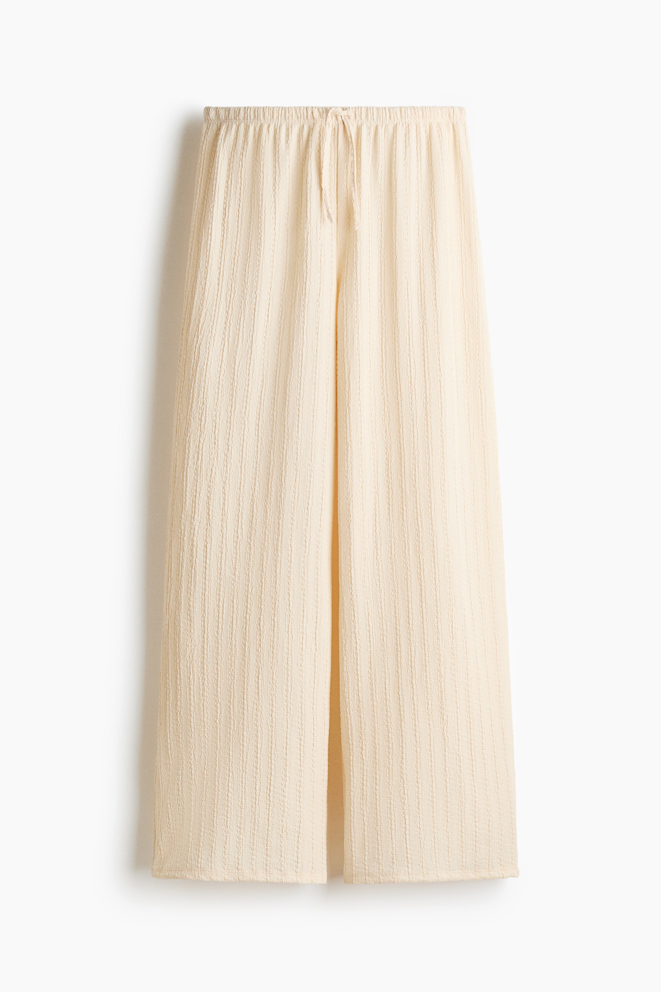 View larger image: The light cream pants are featuring a subtle vertical textured pattern. They are designed with a wide-leg silhouette and an elasticated waistband with a visible drawstring tie at the front.