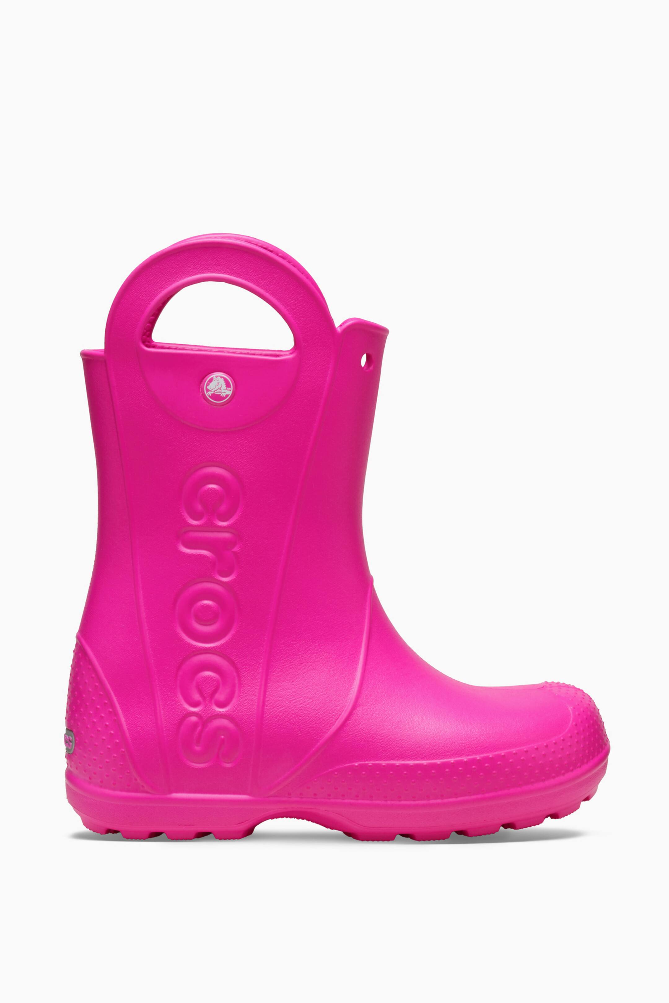 Größeres Bild anzeigen: Ein heißer pinker Crocs-Regenschuh präsentiert seine äußere Seitenansicht, zeigt nach rechts und verfügt über einen mittelkalbigen Schaft mit integrierten Ziehgriffen oben. Der Stiefel zeigt das Wort 'Crocs', das entlang der Seite vertikal eingeprägt ist, ein kleines rundes Crocs-Logo in der Nähe des oberen Griffs, eine strukturierte Zehen- und Fersenpartie sowie eine dicke, geriffelte Sohle.