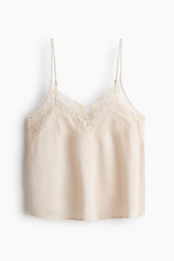 A light beige camisole featuring a V-neckline with intricate lace trim, thin adjustable spaghetti straps, and embroidered detailing positioned below the lace on the front. - 1