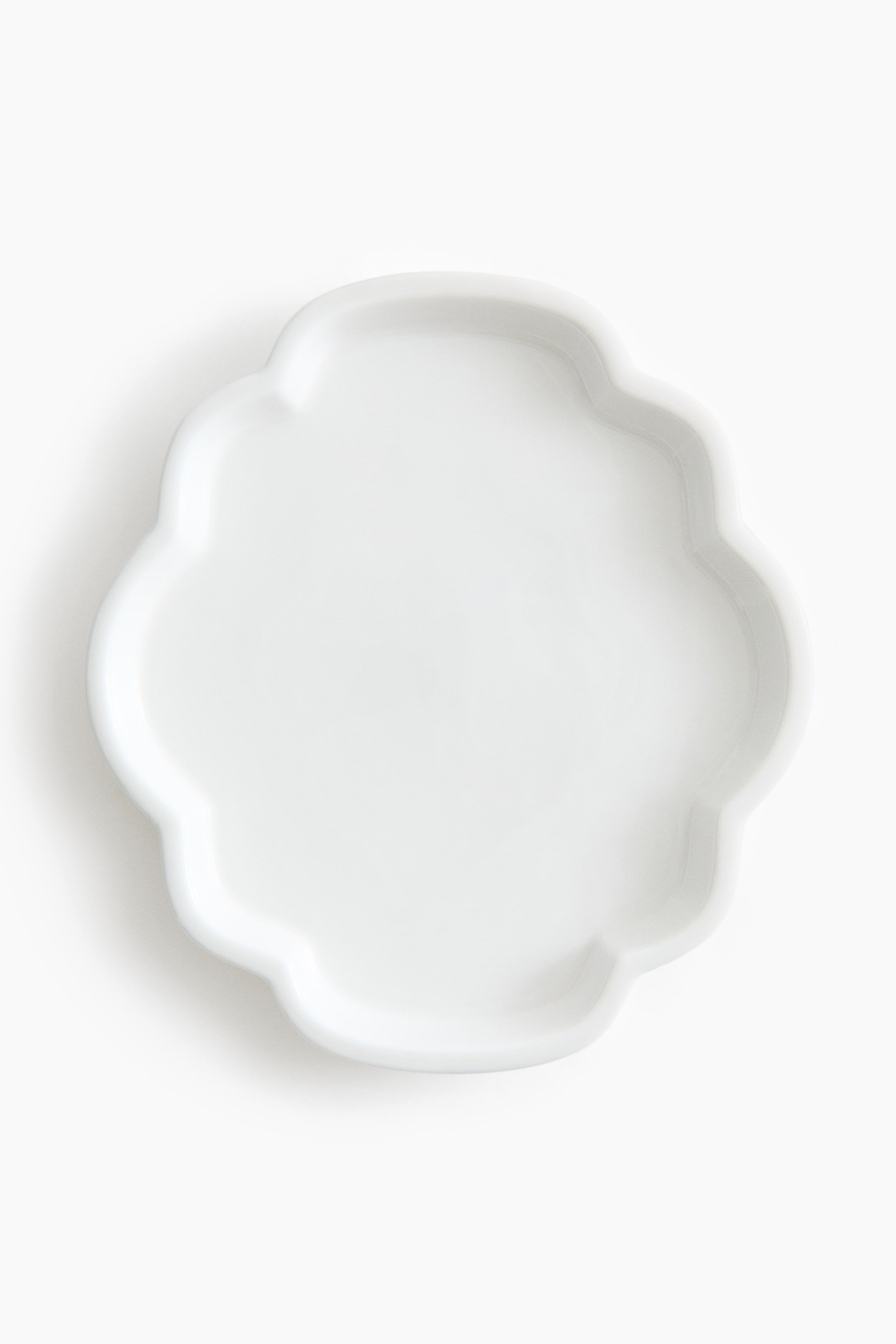 View larger image: A white plate featuring a glossy surface and a scalloped, quatrefoil shape with a slightly raised rim.