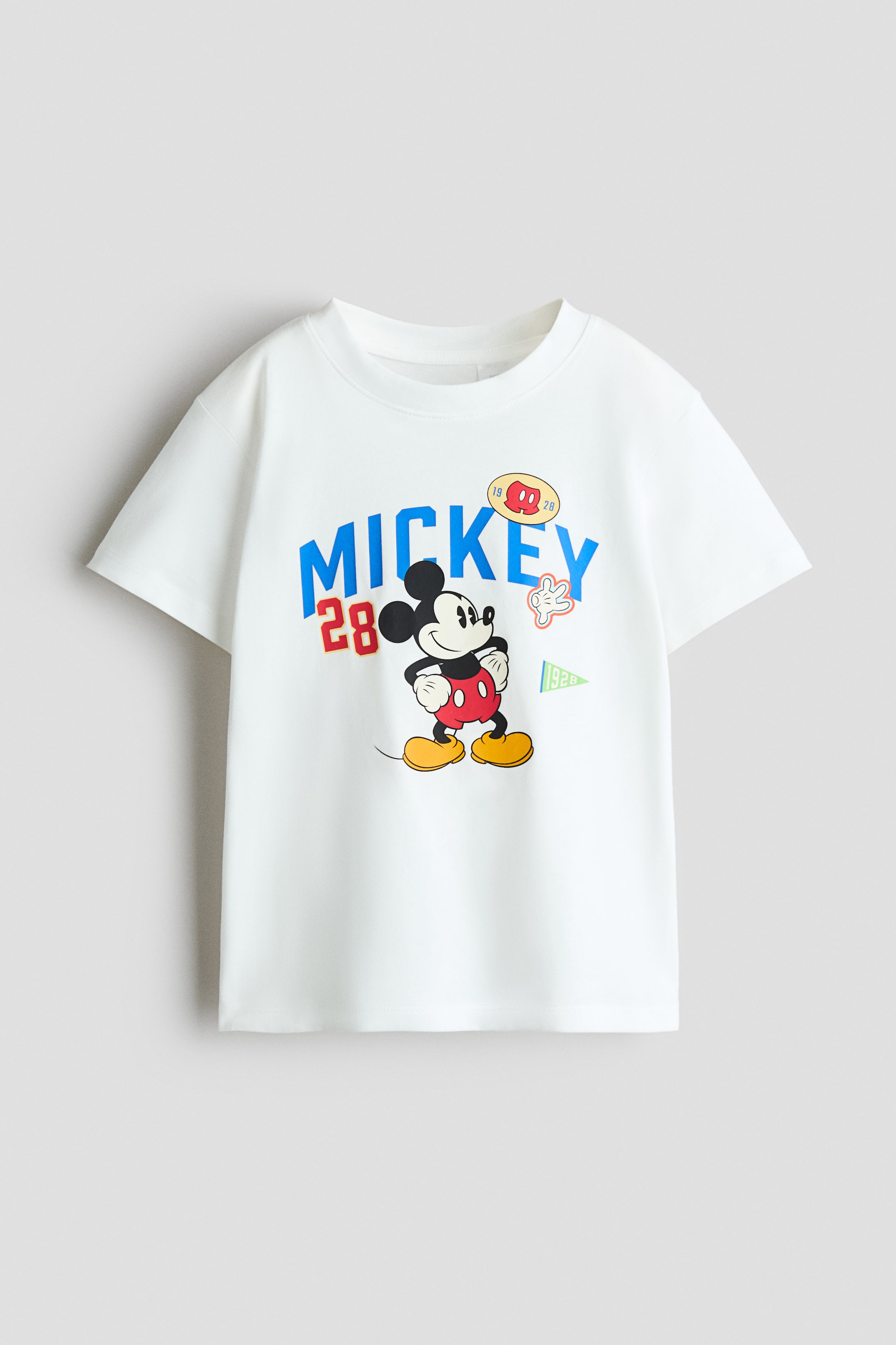 View larger image: A white cotton jersey T-shirt features a printed Mickey Mouse graphic on the front, accented by the word "MICKEY" in blue arched lettering and the number "28" in red. The T-shirt showcases a round, rib-trimmed neckline and short sleeves with gently dropped shoulders.