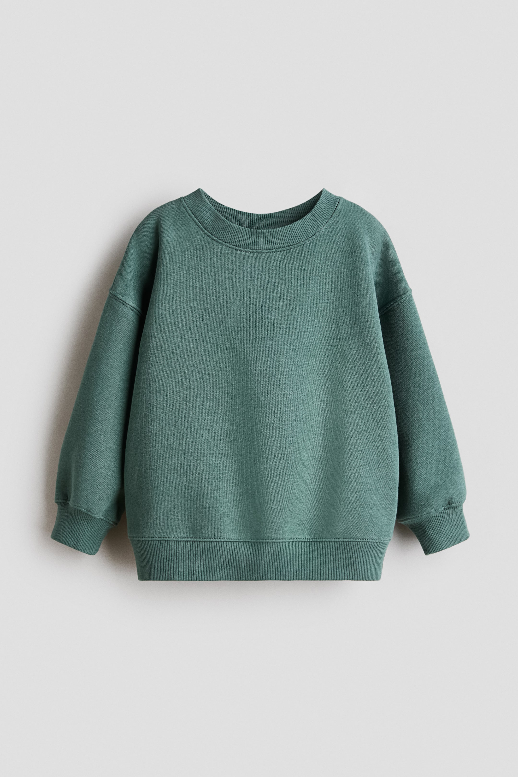 Zobrazit větší obrázek: Oversized mikina v tyrkysové barvě, vyrobená ze sweatshirtového materiálu a zobrazená zepředu (FRONT), má kulatý výstřih s žebrovaným lemem, spadená ramena, dlouhé rukávy, žebrované manžety a žebrovaný spodní lem.
