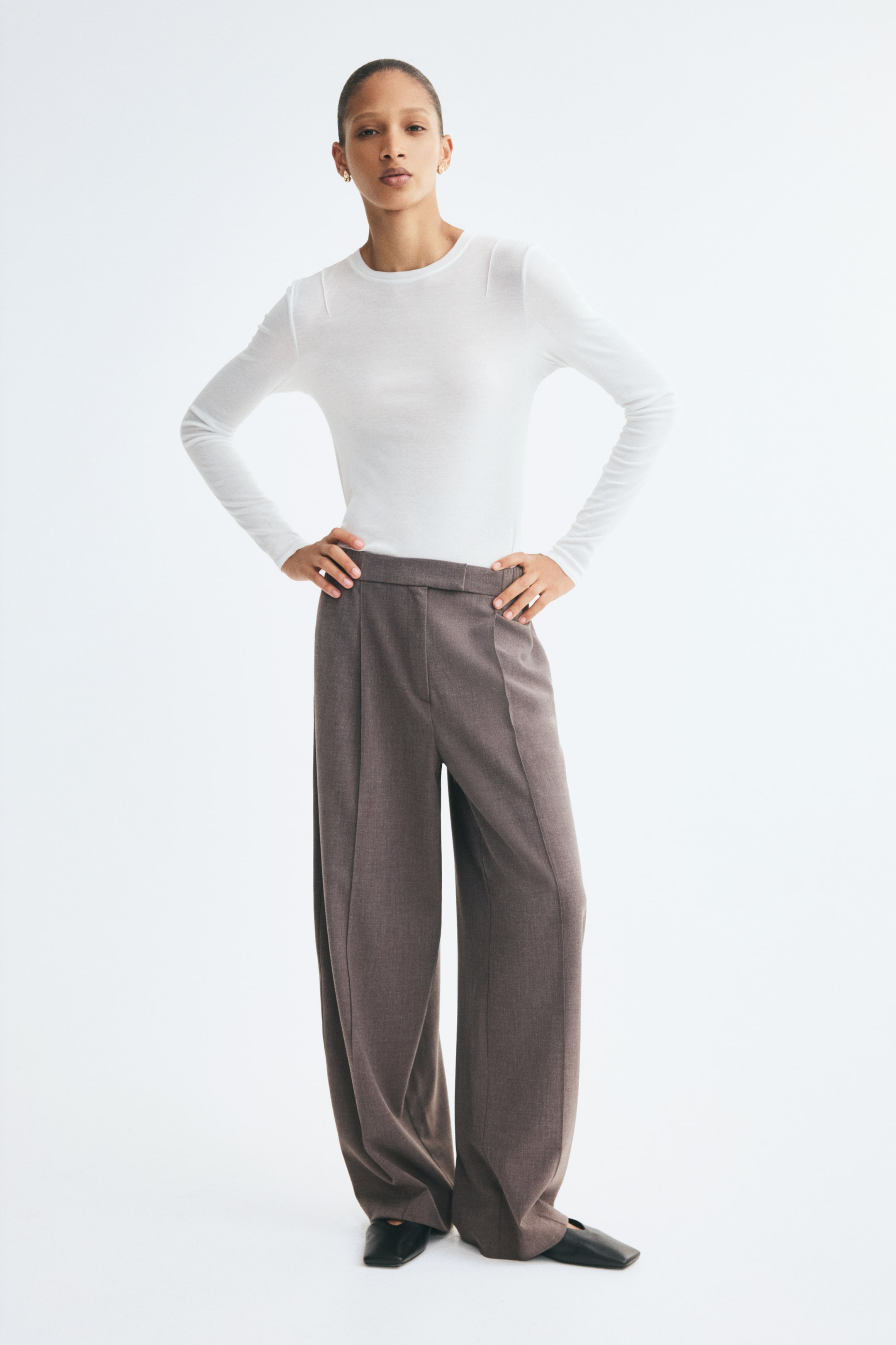 View larger image: Loose-fit, taupe-brown pants in a woven fabric are shown from the front, highlighting a regular waist with an extended waistband. The pants drape into wide barrel legs, featuring prominent front pleats and sharp creases running down the centre of each leg.