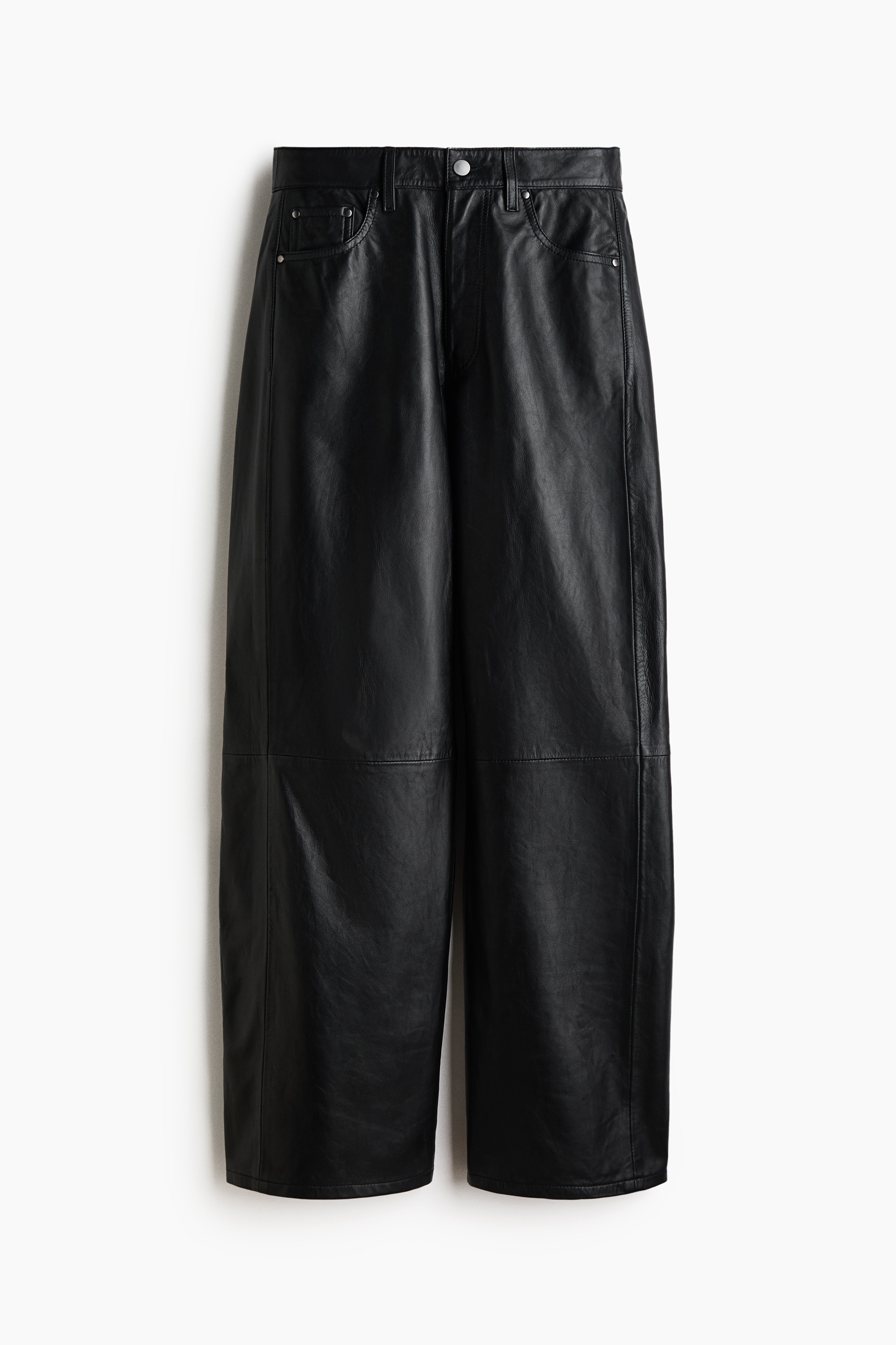 Un pantalon en cuir noir Ã  la coupe ample, taille normale et jambes barrel, avec des coutures horizontales apparentes au niveau des genoux, est portÃ© par le mannequin. Celui-ci pose avec une main dans la poche, associÃ© Ã  un blazer noir court et portant un sac en cuir noir assorti.