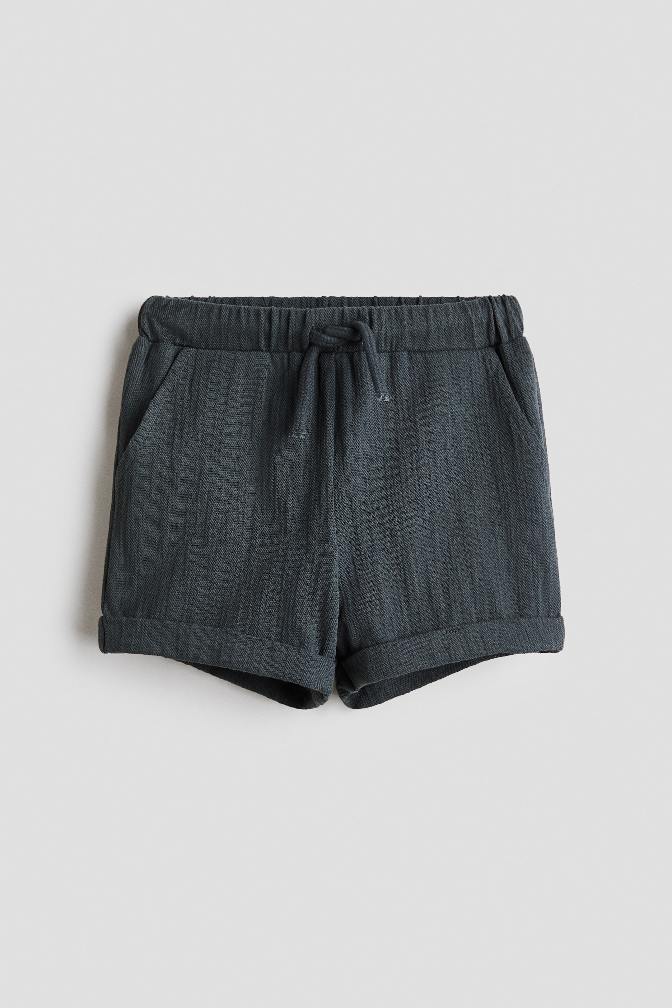 View larger image: The shorts are shown from the front, showcasing a dark grey shade with a subtle vertical textured pattern. They feature an elastic waistband with a front drawstring, two side pockets, and rolled-up hems.