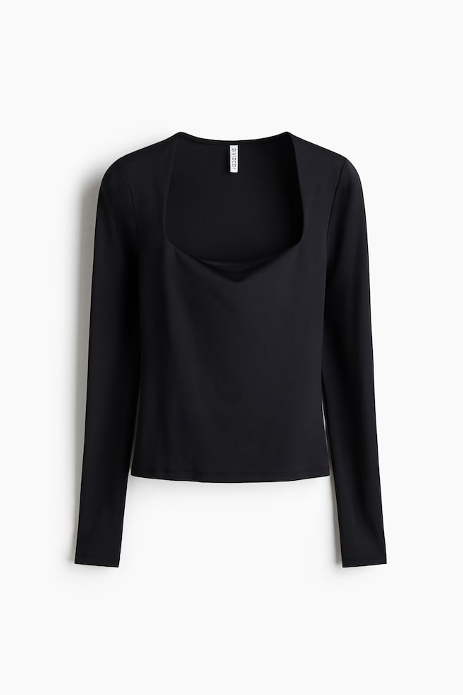 A black long-sleeved top is presenting a front view, featuring a square neckline with a slight cowl drape. It is designed with long sleeves and a straight hem, and a small white "DIVIDED" tag is visible at the back of the neckline. - 1