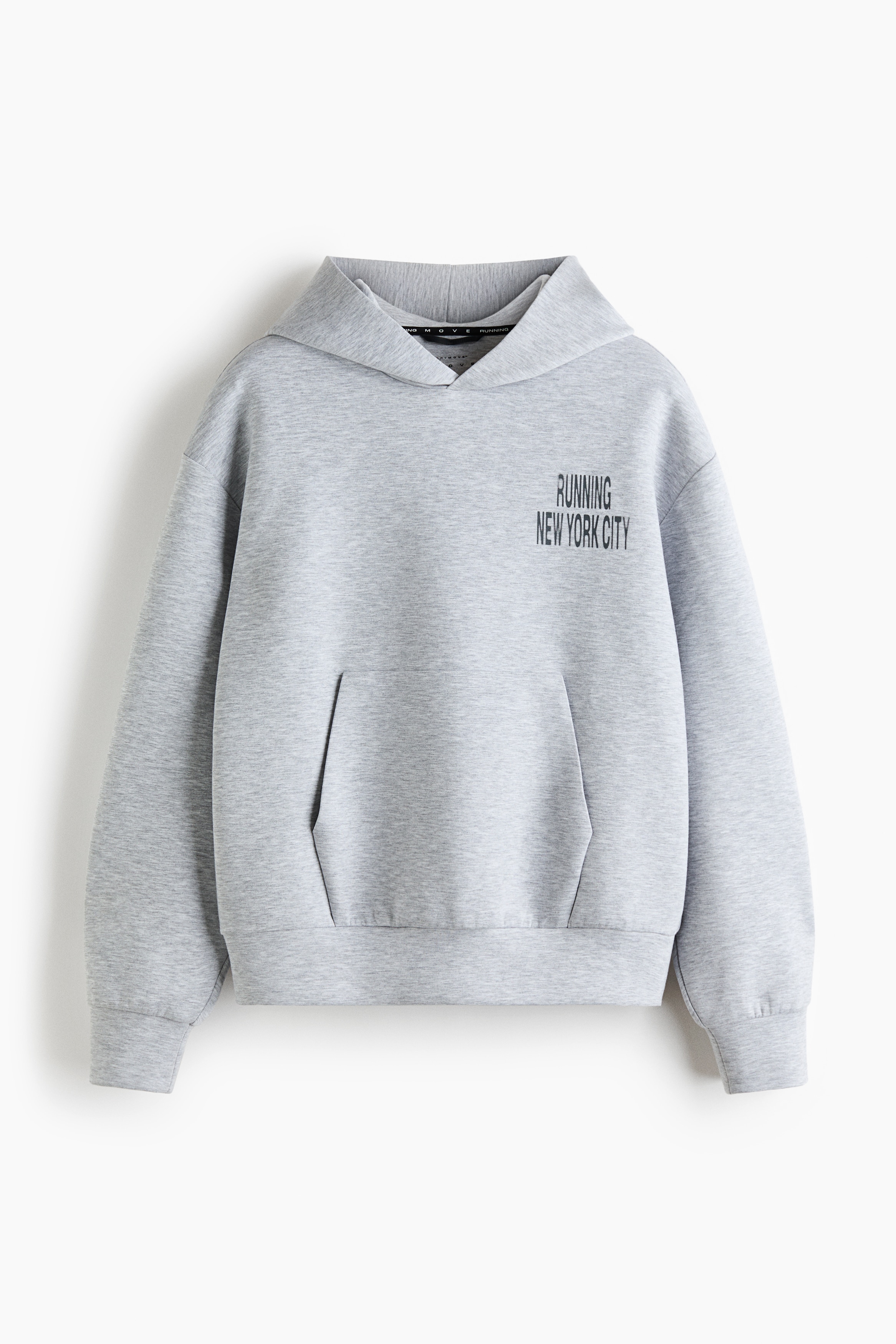A light grey, oversized hoodie featuring a front kangaroo pocket and black graphic text on the left chest is being worn by the model, who is placing both hands inside the pocket. The hoodie is styled with bright blue, form-fitting athletic shorts.