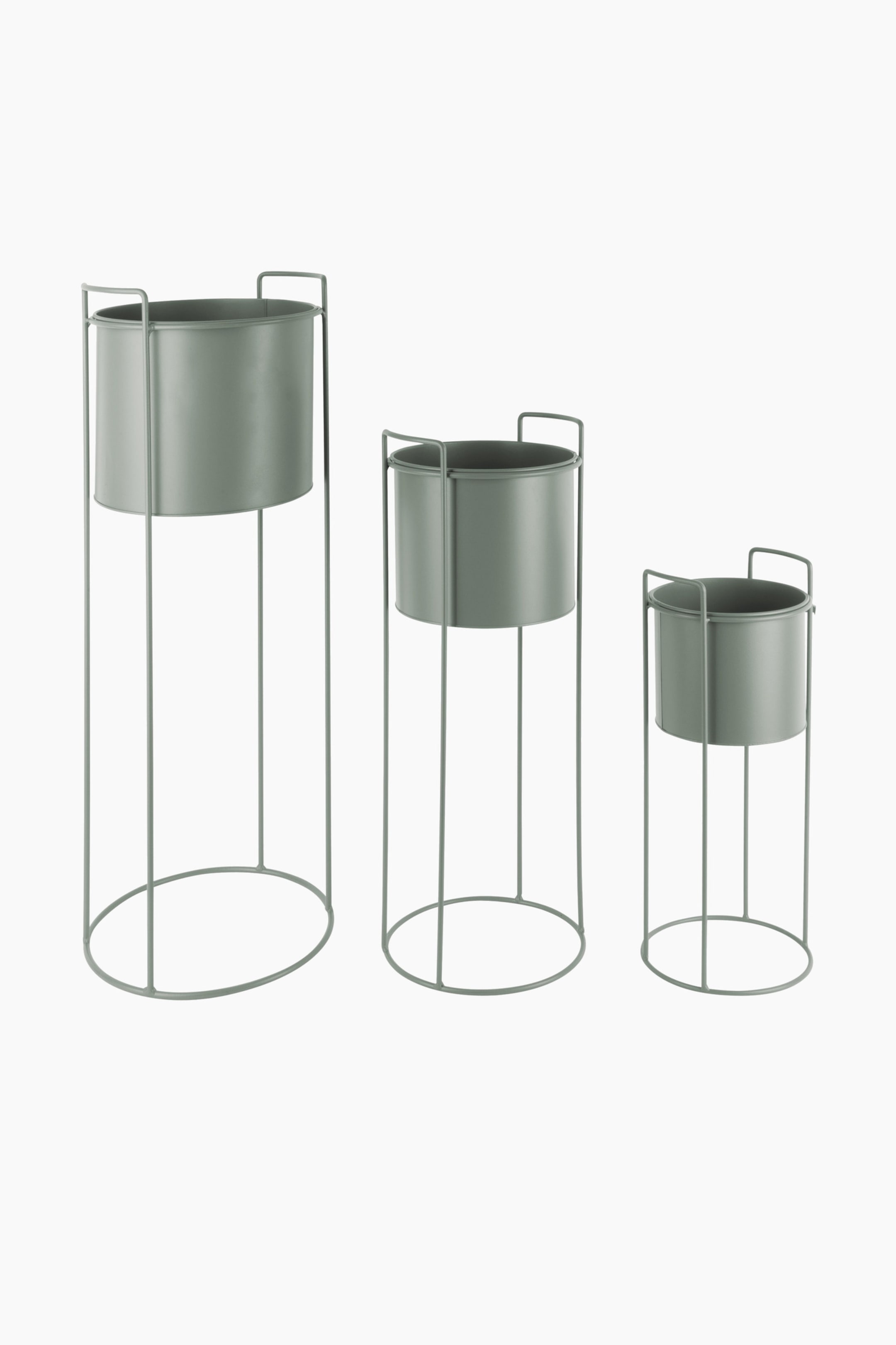 Grotere afbeelding bekijken: Drie cilindrische plantenstandaards worden gepresenteerd onder een lichte hoek naar rechts-voor, variërend in hoogte. Elke standaard draagt een gedempte groene pot die wordt ondersteund door een bijpassend minimalistisch draadframe, dat een cirkelvormige basis, verticale steunen en twee kleine lussen vormt die omhoog steken vanaf het frame bij de rand van de pot.