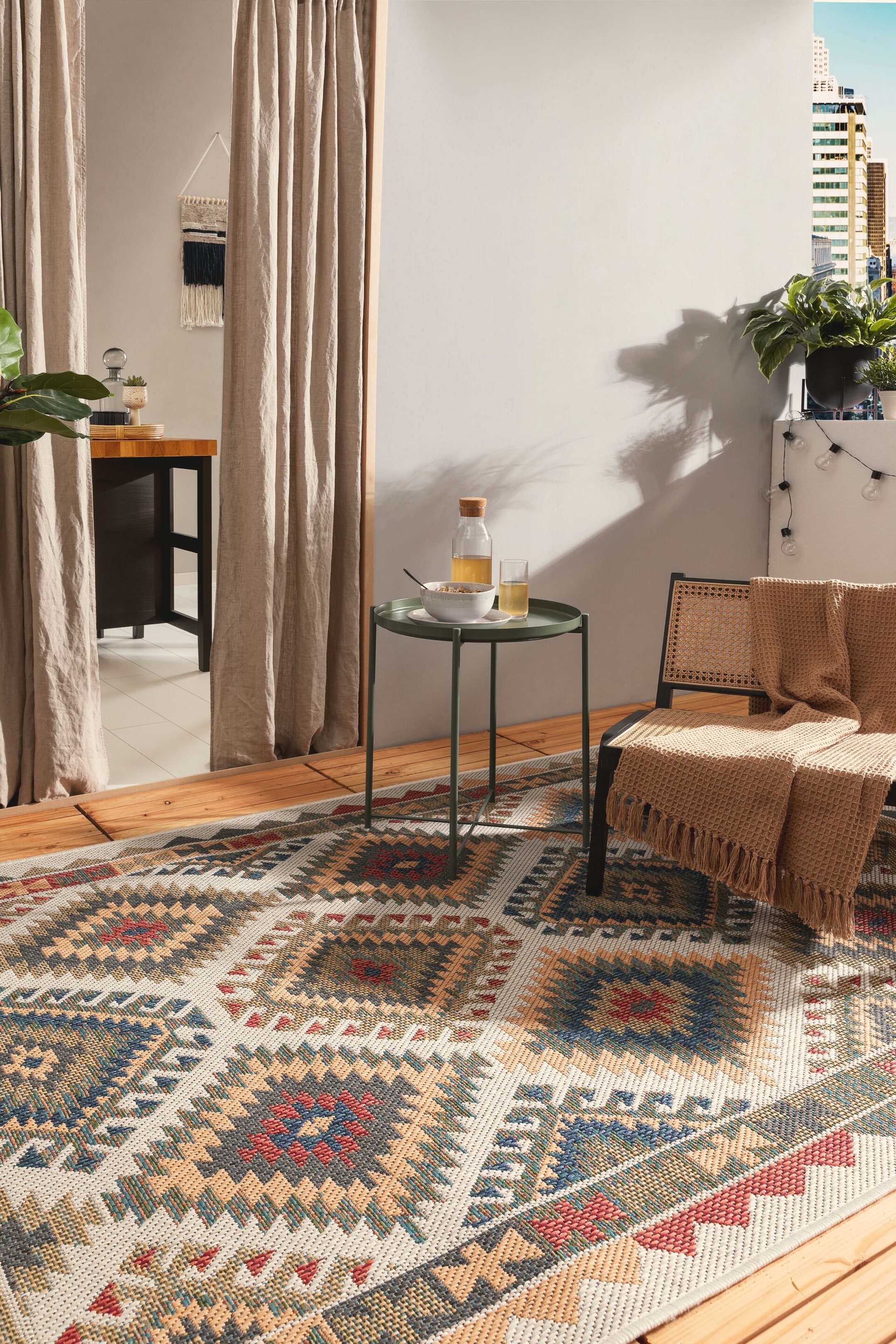 Visa större bild: Mattan visar upp ett geometriskt mönster i flera toner, med upprepade diamant- och triangulära motiv i nyanser av rött, blått, gyllengult, olivgrönt och ljusgrått. Den ligger plant på ett trägolv, delvis synlig och sträcker sig mot betraktaren.