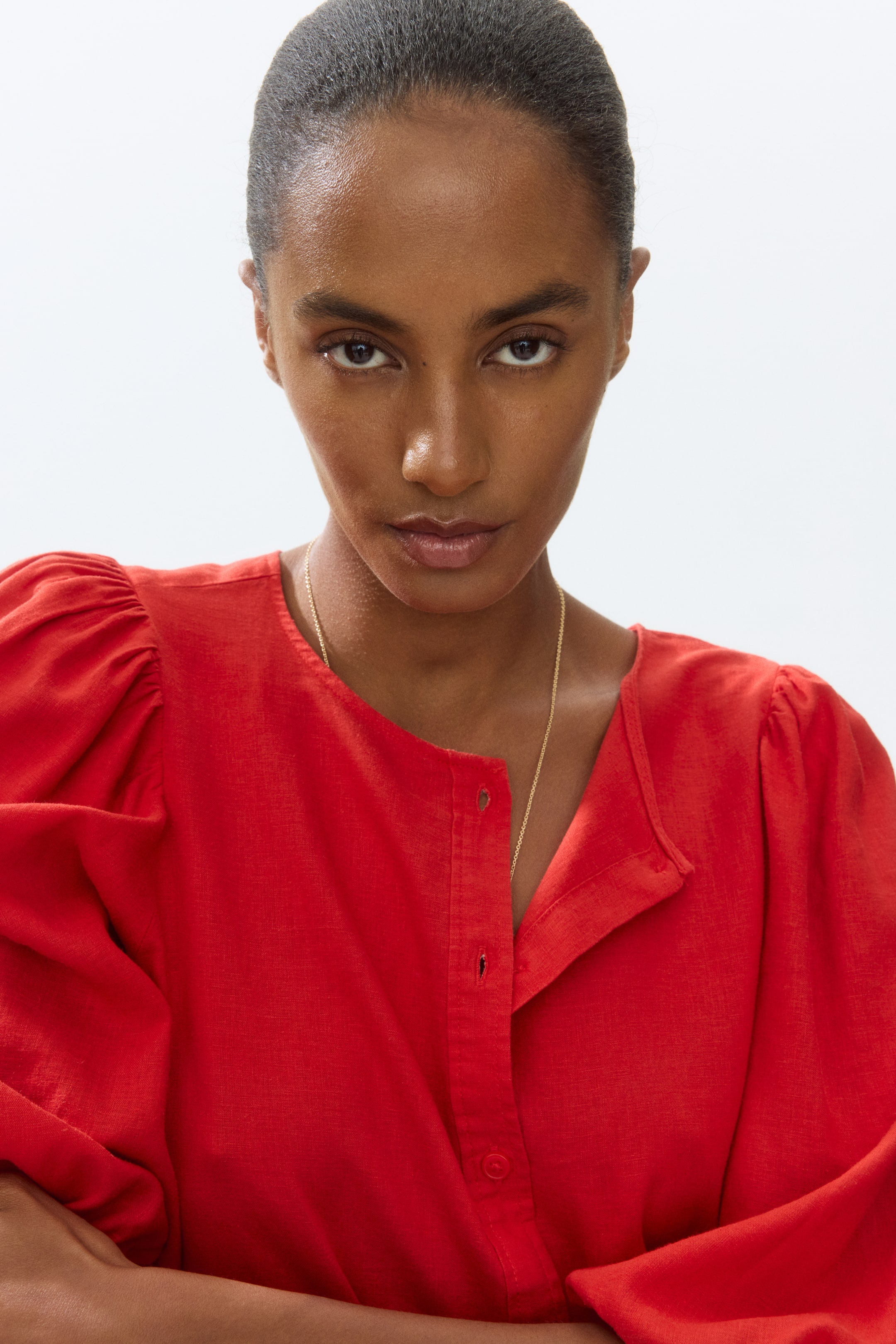 View larger image: The red top showcases puffed sleeves and a collarless neckline, complemented by a partial button placket adorned with petite red buttons and a textured fabric weave.