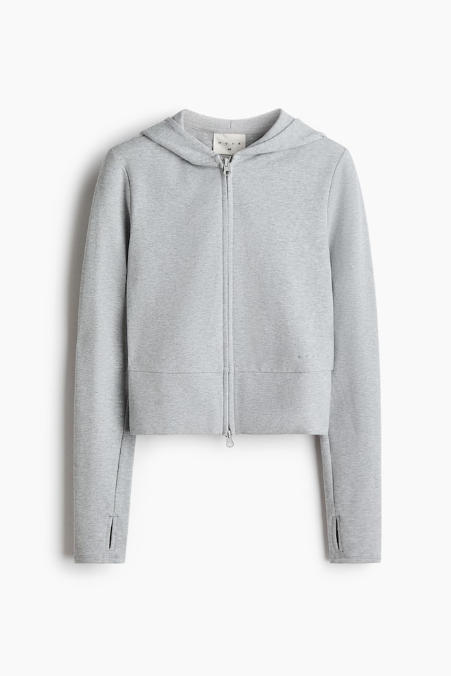 A light grey melange cropped zip-up hoodie is shown from the front, featuring an attached hood, a two-way front zip, and long sleeves with thumbhole cuffs. The design includes a wide panelled hem and subtle tonal branding on the lower left side. - 1