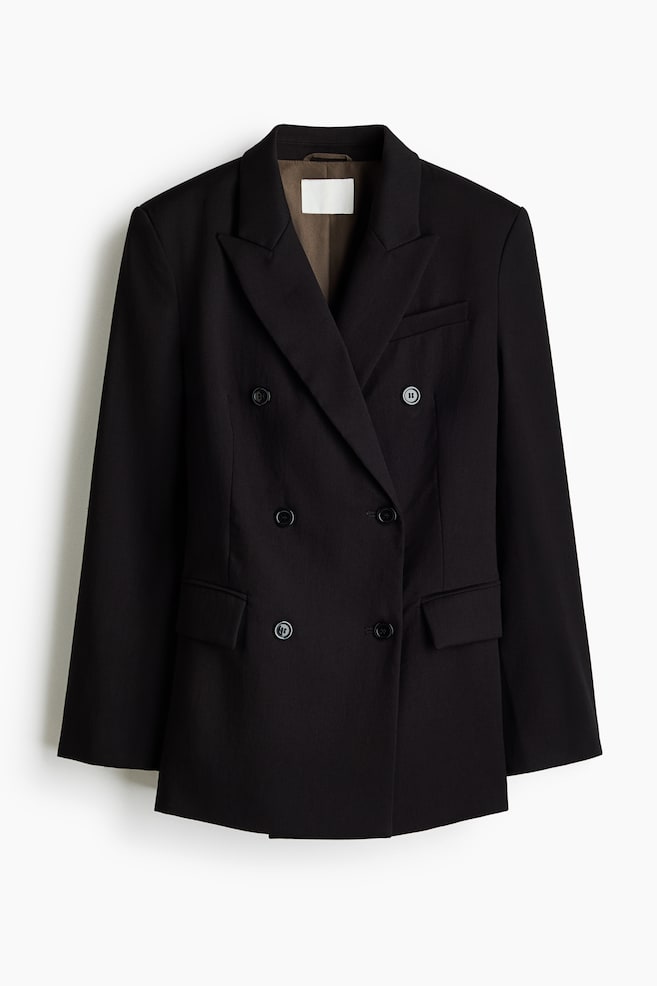 A black, double-breasted blazer is hanging facing front, featuring structured shoulders, peak lapels, and a six-button front closure. The long-line design includes a single welt chest pocket, two lower flap pockets, and a contrasting brown lining visible at the neckline. - 1