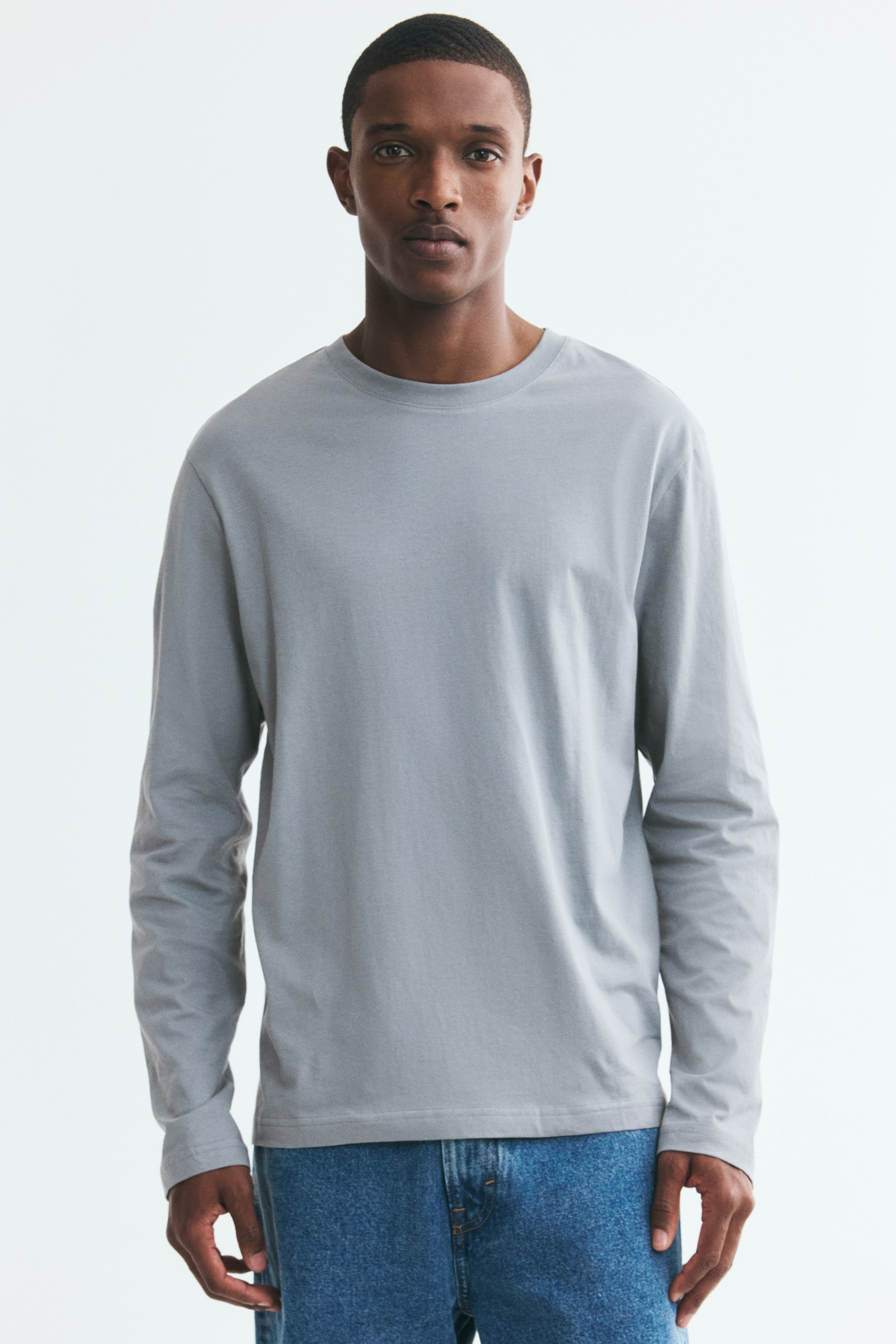Ver imagen más grande: Un top de manga larga en color gris claro con un cuello redondo ribeteado, mangas largas y un dobladillo recto está siendo llevado por la modelo. El top presenta un ajuste regular.