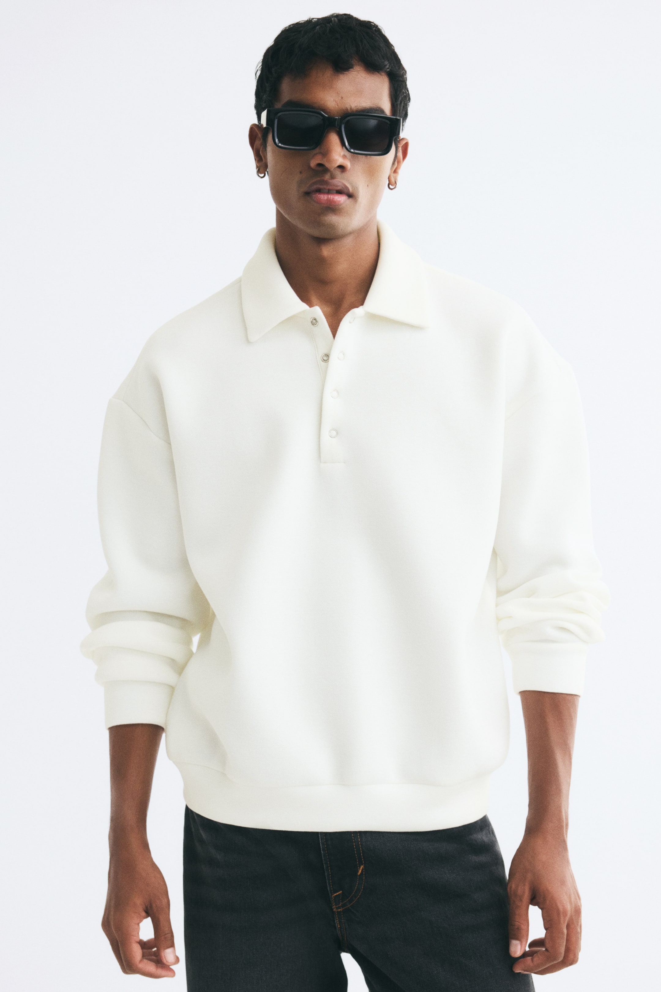 View larger image: The model is wearing an off-white oversized polo shirt in structured scuba fabric. The shirt features a classic collar with silver press-stud fasteners, dropped shoulders, long sleeves, and a banded hem.