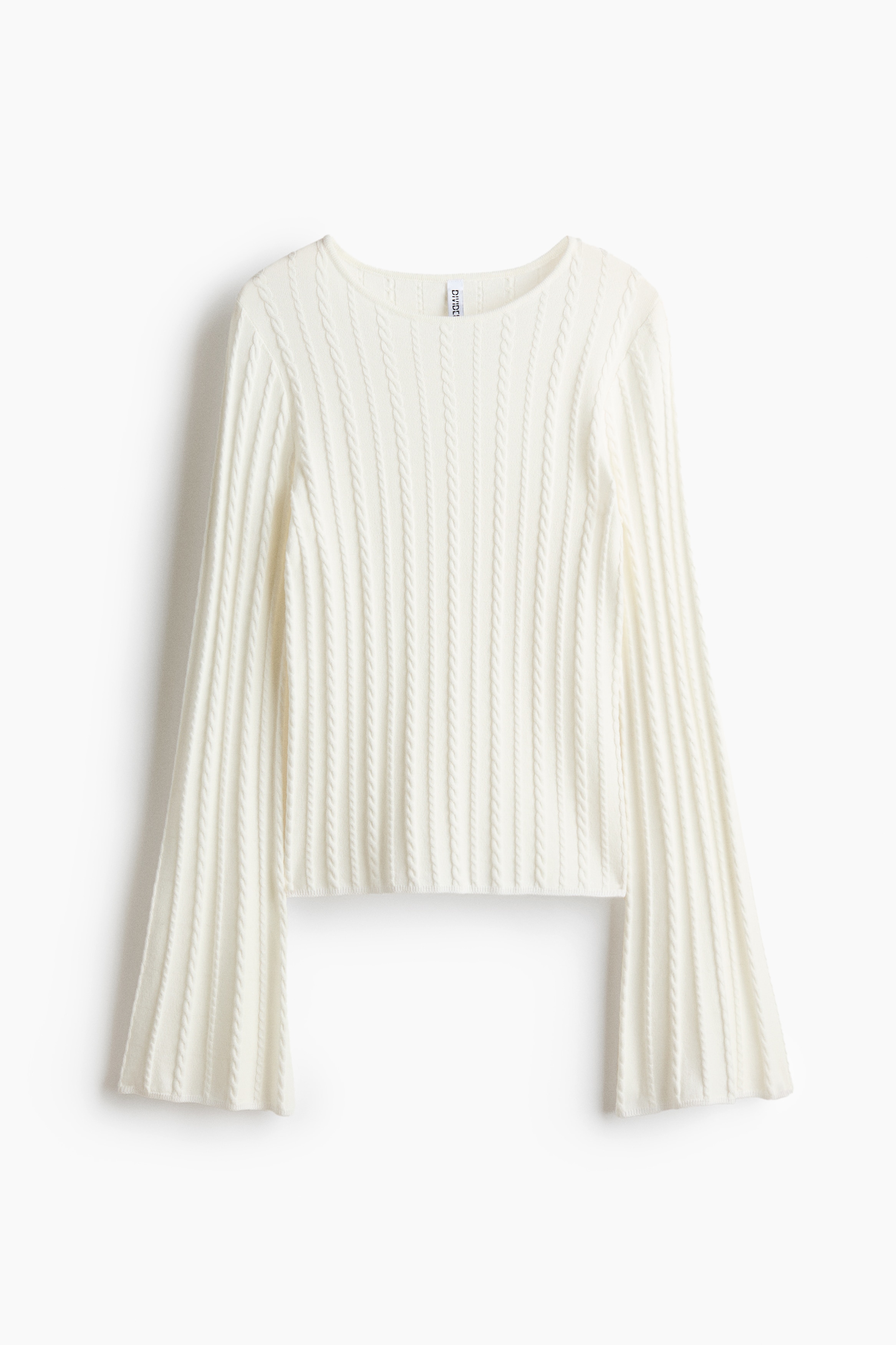 Een crÃ¨mekleurige kabelgebreide top met ronde hals en lange mouwen wordt gedragen door het model. De top is gestyled met een zwarte leren rok en bijpassende kniehoge laarzen terwijl het model zit.