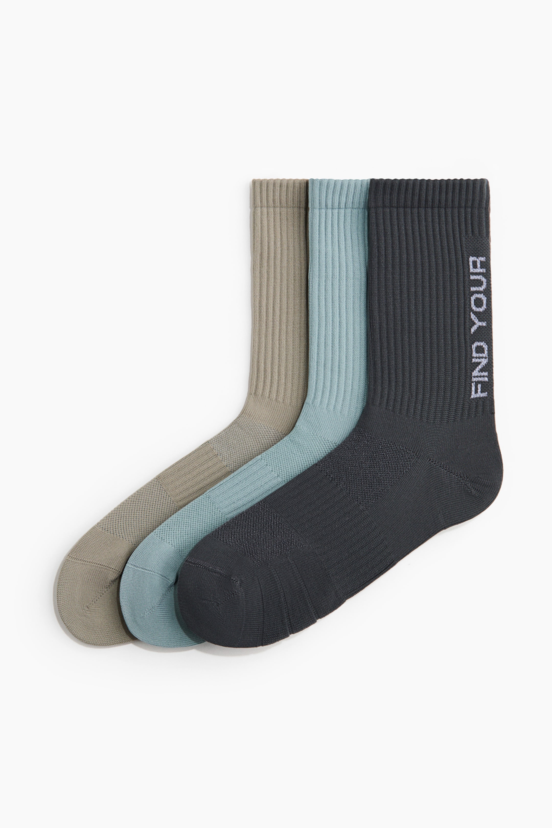 View larger image: A 3-pack of sports socks is showcasing three colours: taupe, light blue, and charcoal grey, arranged side-by-side. Each sock features a ribbed cuff and a textured knit on the foot and lower leg, with the charcoal grey sock displaying "FIND YOUR" printed vertically in white on its outer side.