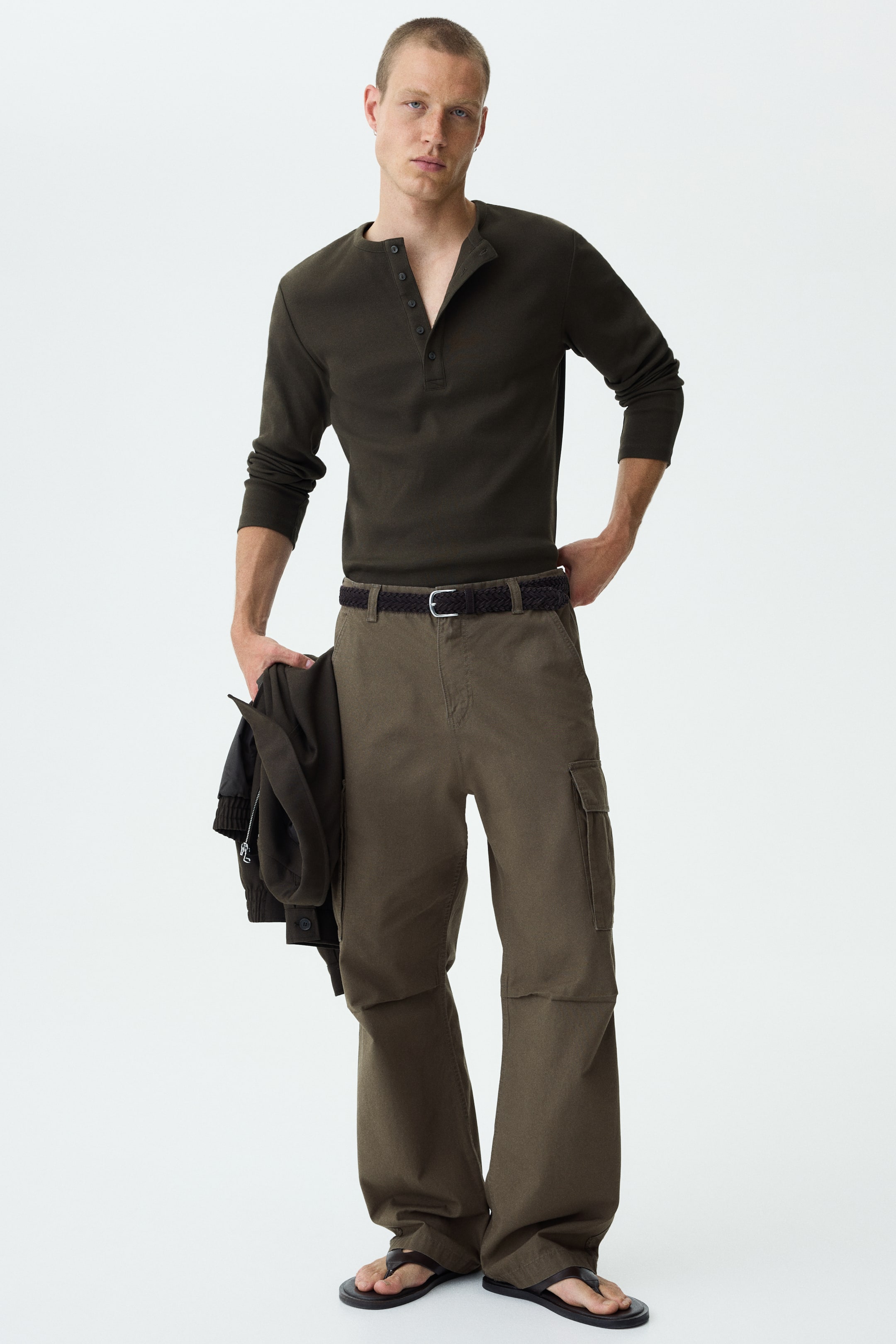 Agrandir l'image: Les pantalons cargo vert olive présentent une coupe décontractée à jambes larges, vus de face. Ils affichent de grandes poches cargo sur les côtés des cuisses, des détails de couture aux genoux, et un large ourlet tombant librement sur les pieds.