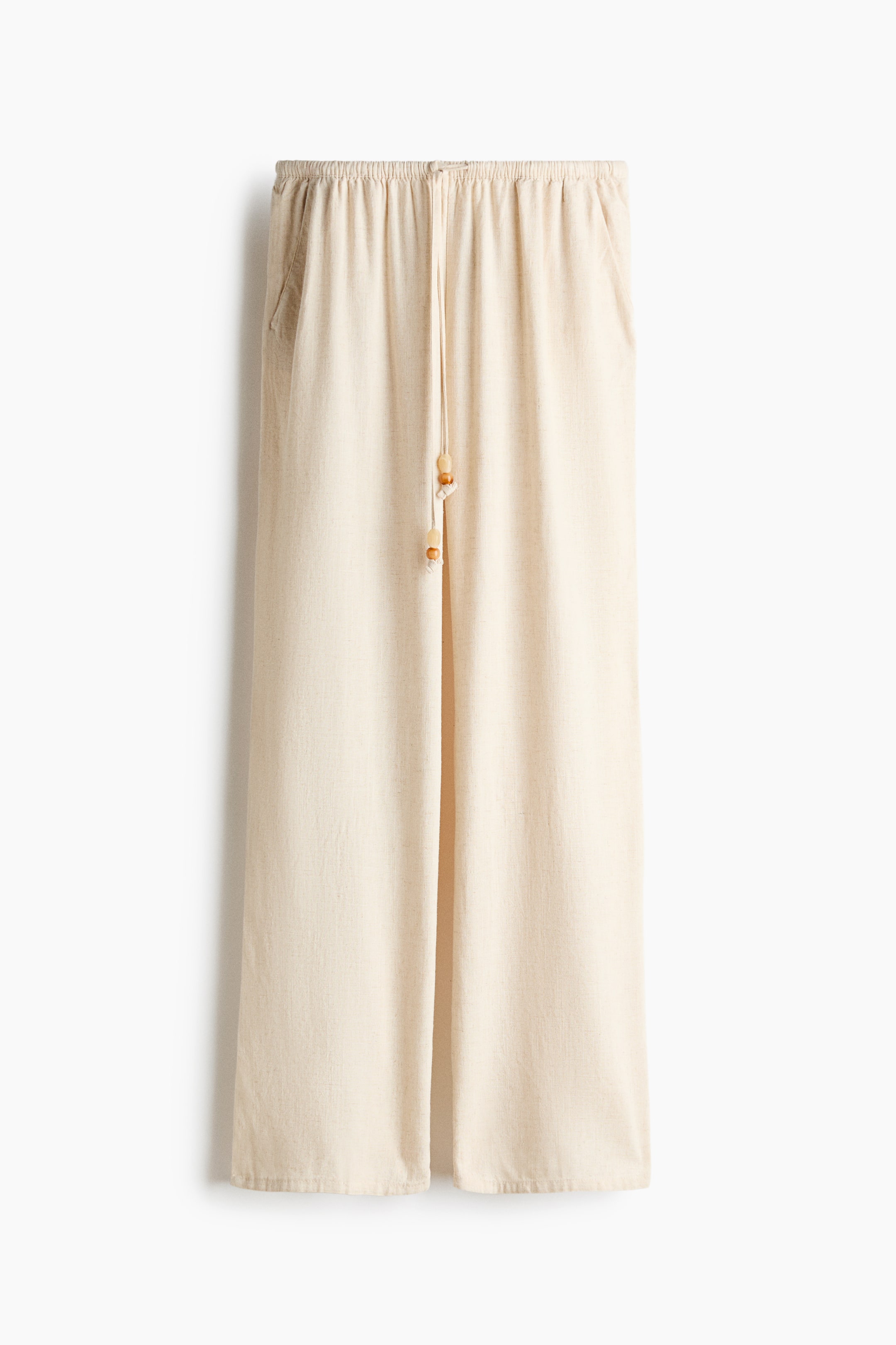View larger image: Light beige trousers with an airy weave are showcased from the front, featuring a low elastic waistband with a drawstring accented by two wooden beads, diagonal side pockets, and straight legs.