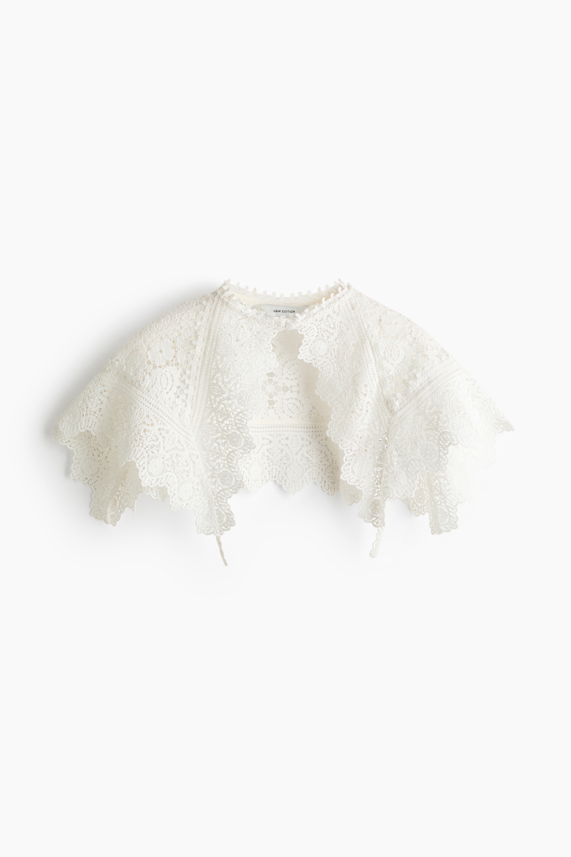 Un large col blanc en dentelle effet crochet Ã  bords festonnÃ©s est portÃ© par le mannequin, retombant sur les Ã©paules dâune blouse blanche Ã  col montant. Le col prÃ©sente des motifs ajourÃ©s raffinÃ©s et est associÃ© Ã  un jean noir.